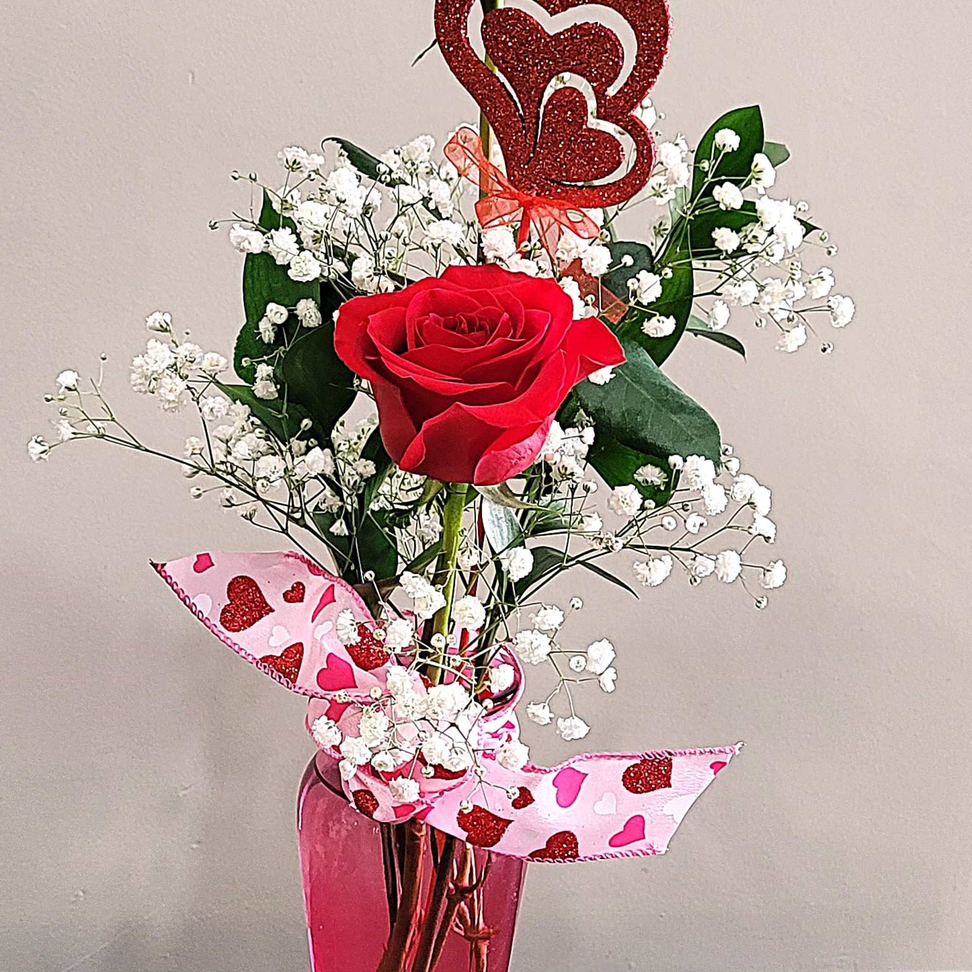 Tall pink vase with two red roses, baby’s breath, and a glitter heart pick