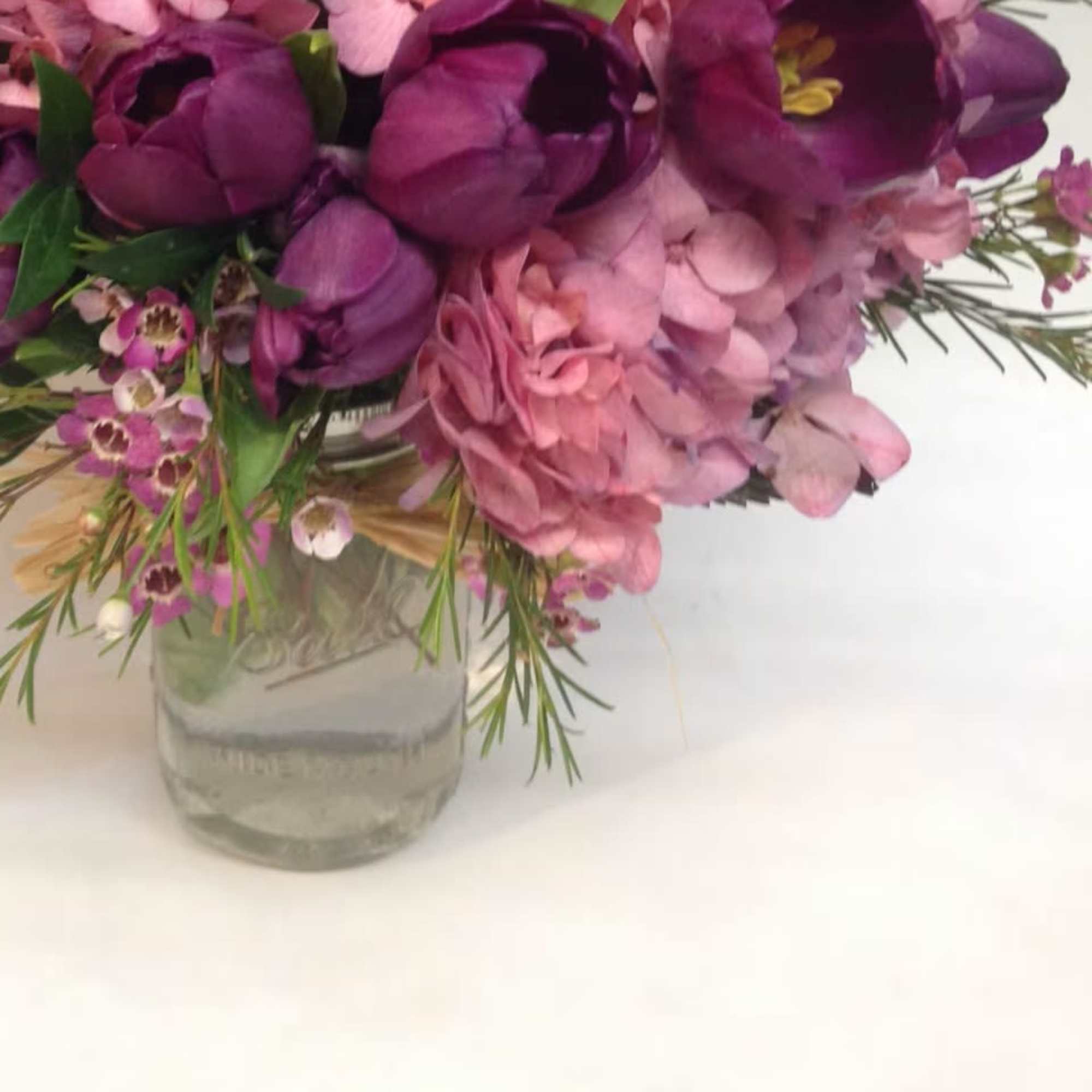 Purple and pink flowers arranged in a clear glass jar vase