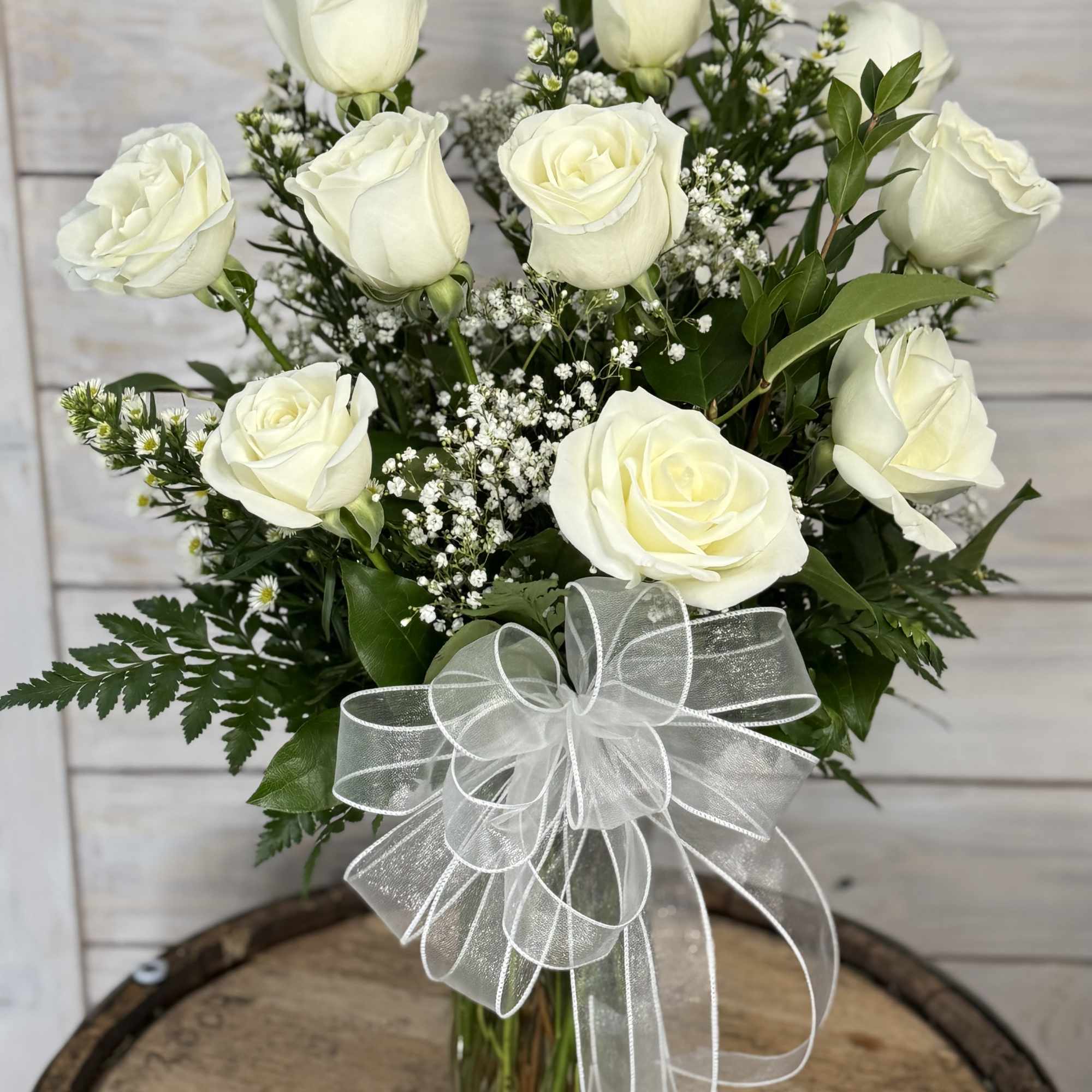 White roses in a clear glass vase with a sheer white bow