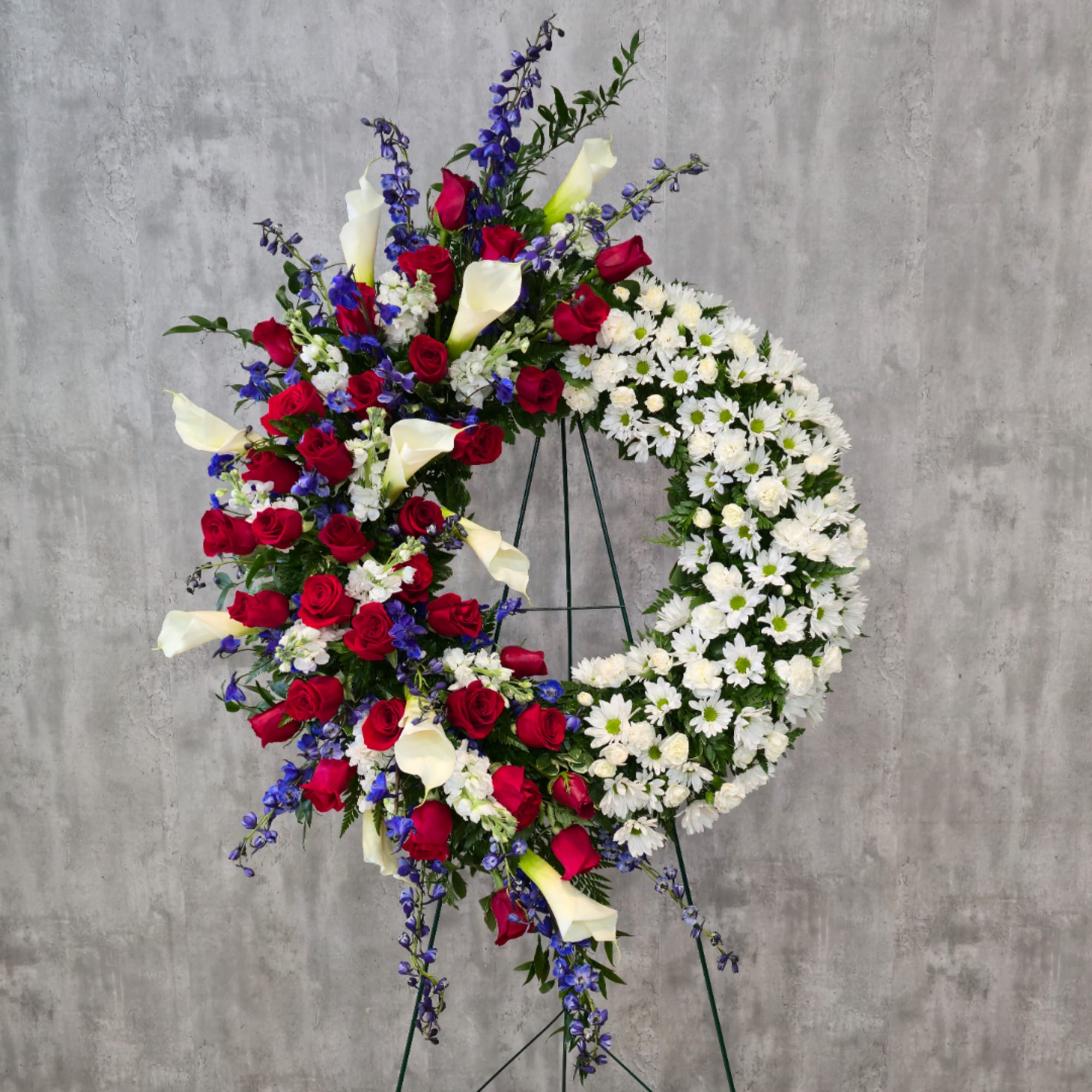 Large standing floral wreath with red roses, white calla lilies, and white daisies