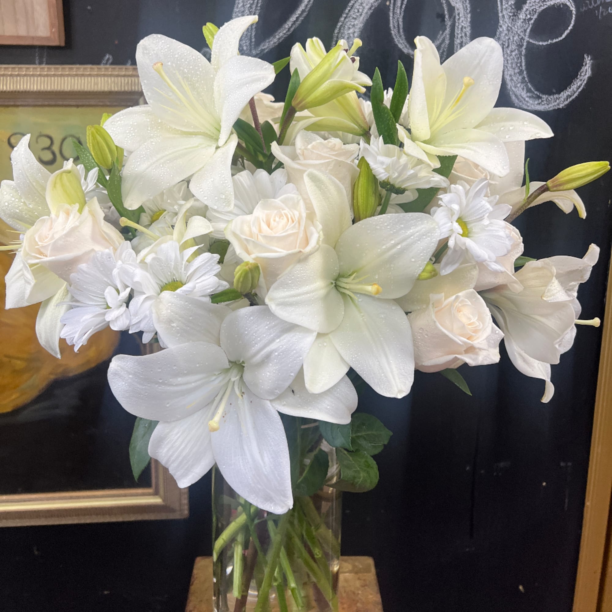 White lilies, roses, and daisies arranged in a clear glass vase