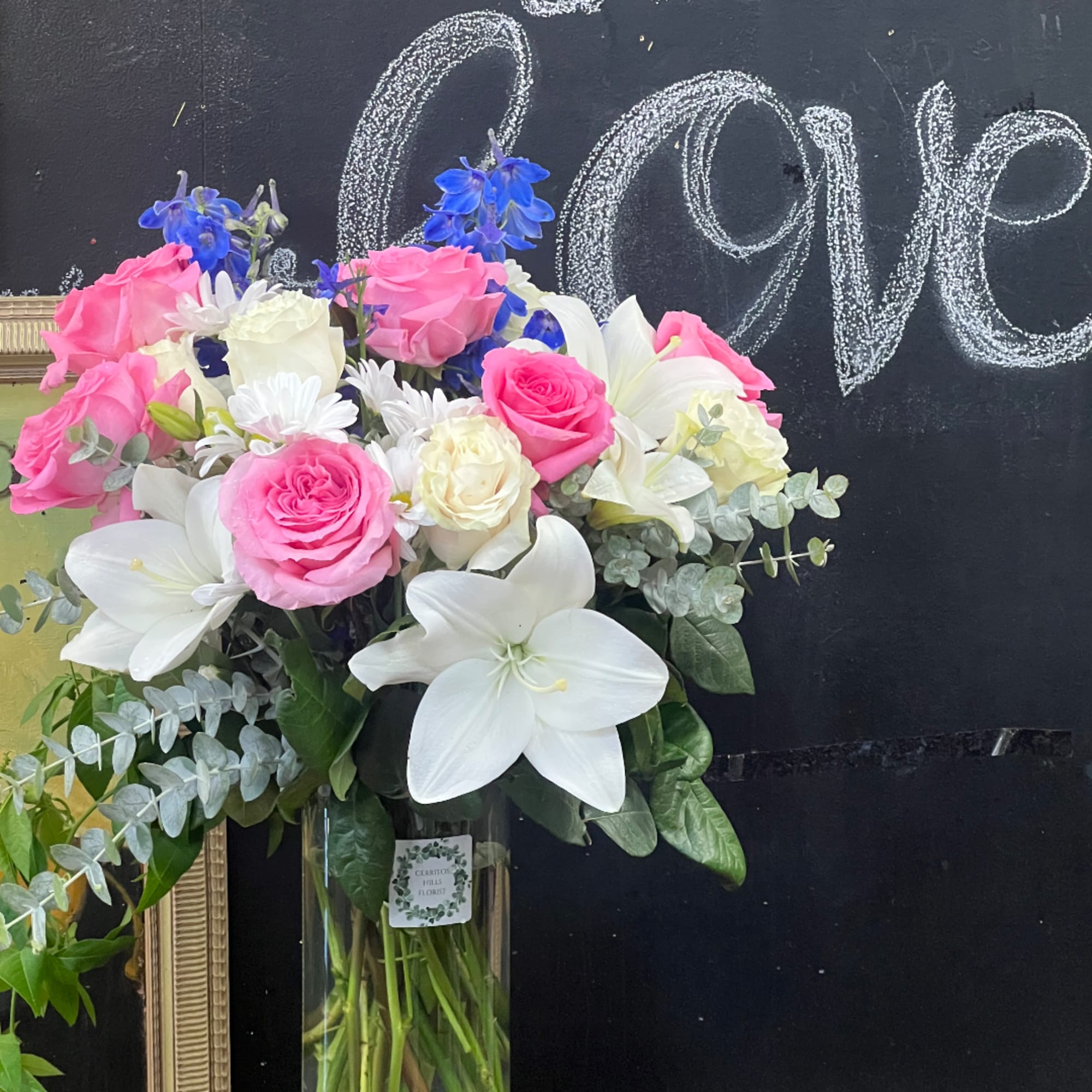Bouquet of pink and white roses with lilies and blue flowers in a glass vase