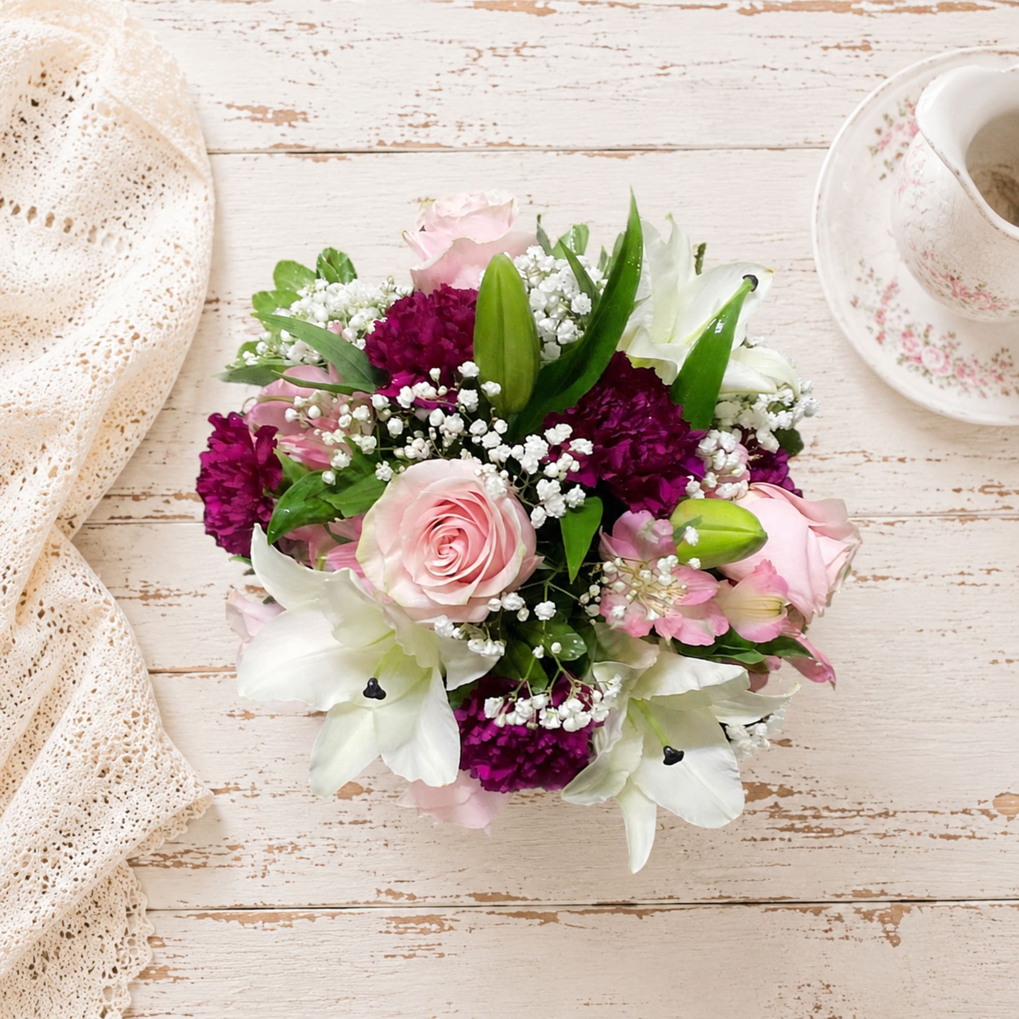 Pink roses and white lilies arranged with purple flowers on a rustic table