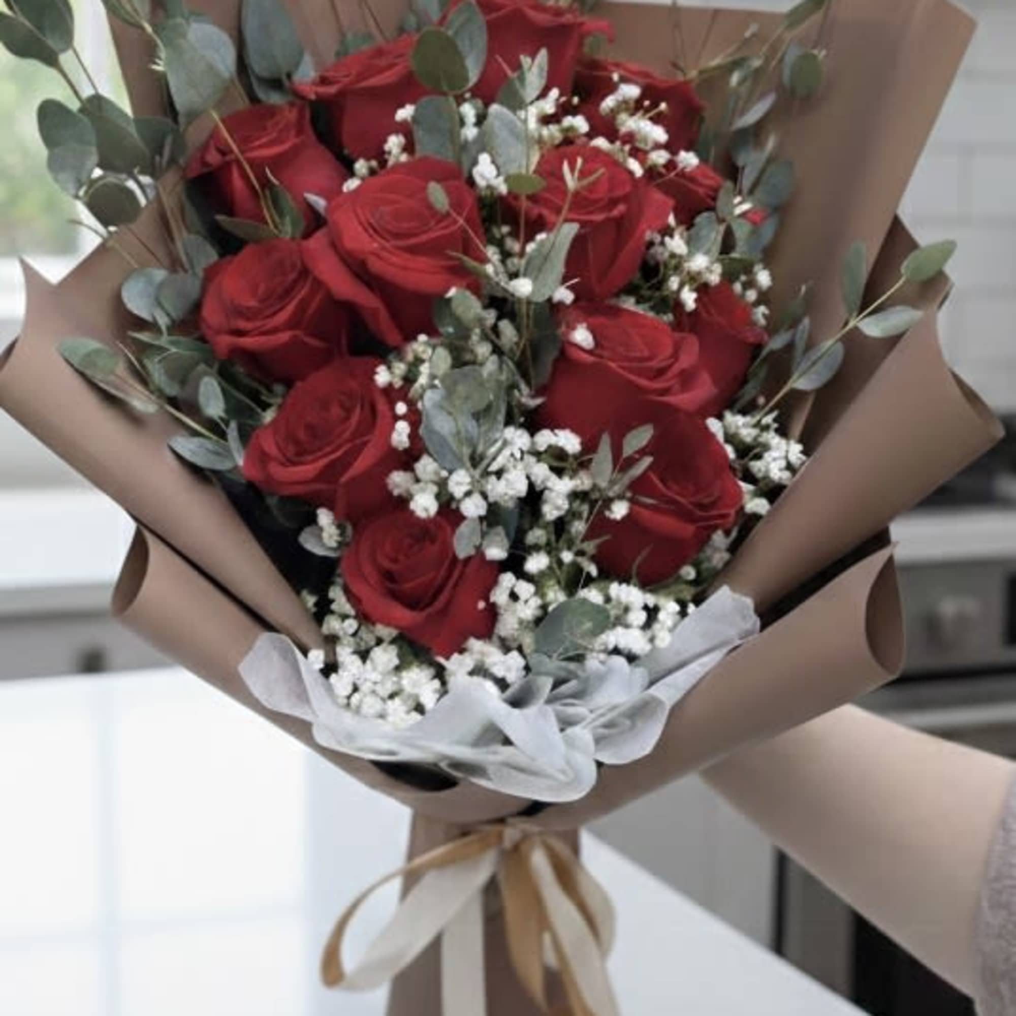 Bouquet of red roses with white filler flowers and eucalyptus in brown paper