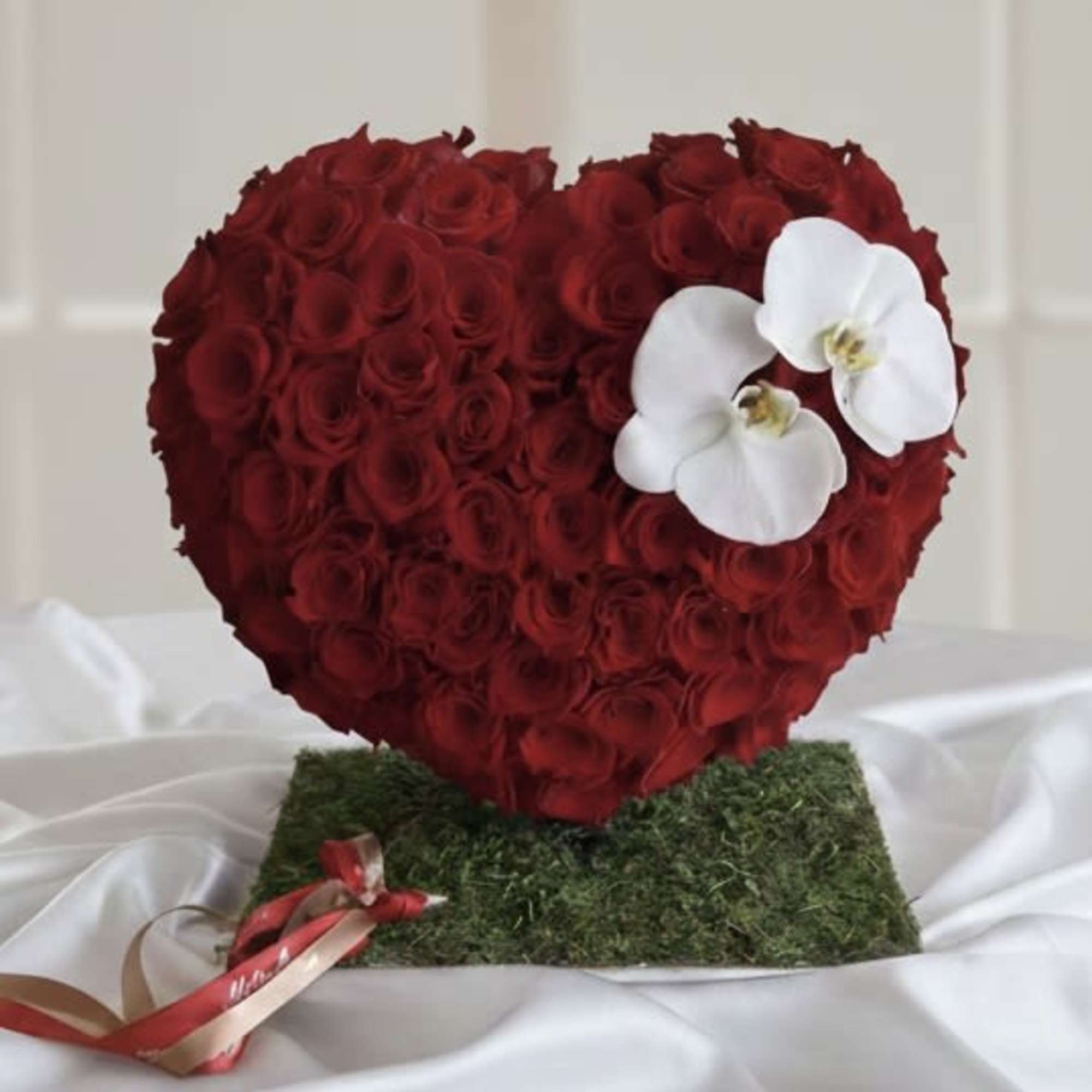 Heart-shaped red rose arrangement with white orchids on a moss base