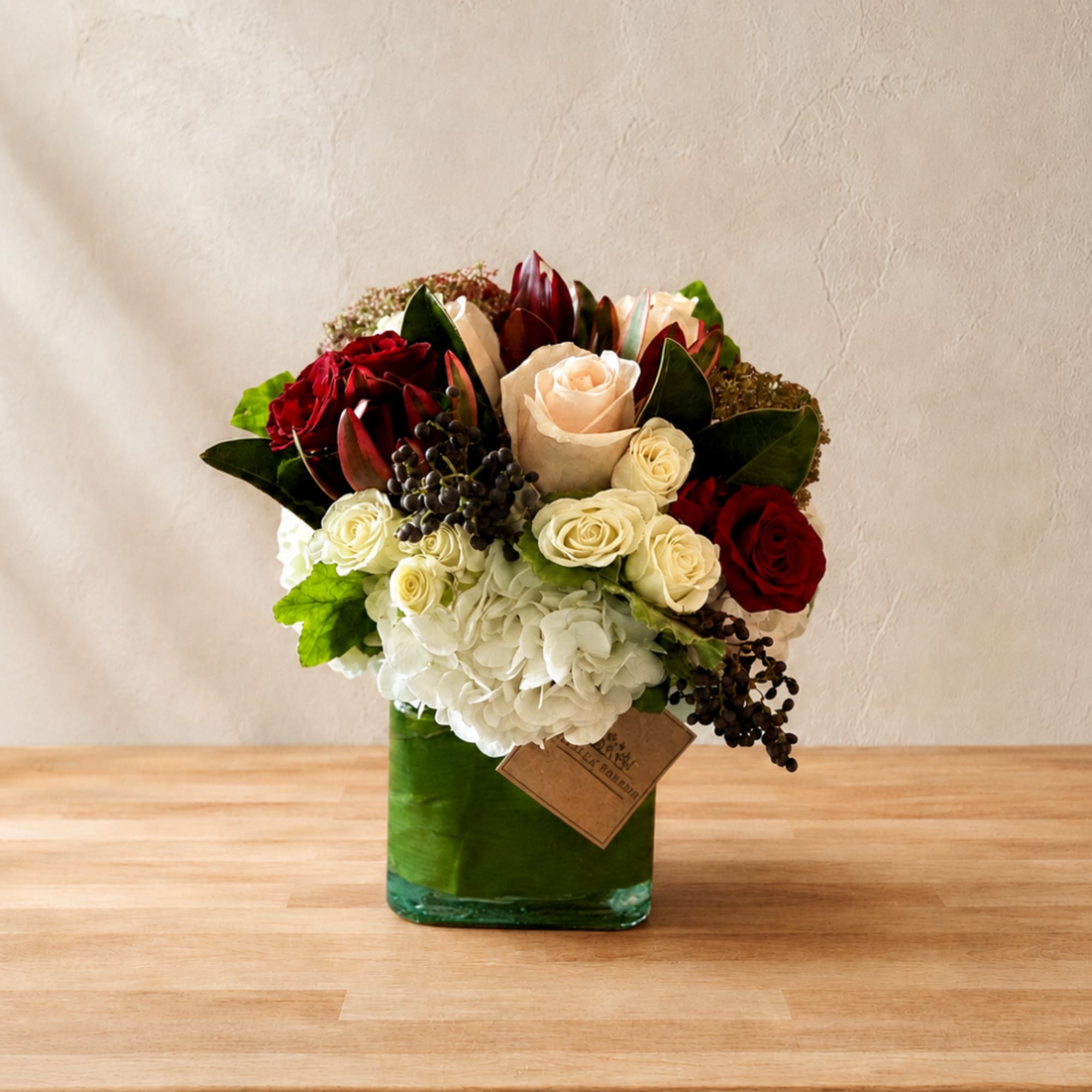 Mixed rose arrangement in a green glass vase with white hydrangea