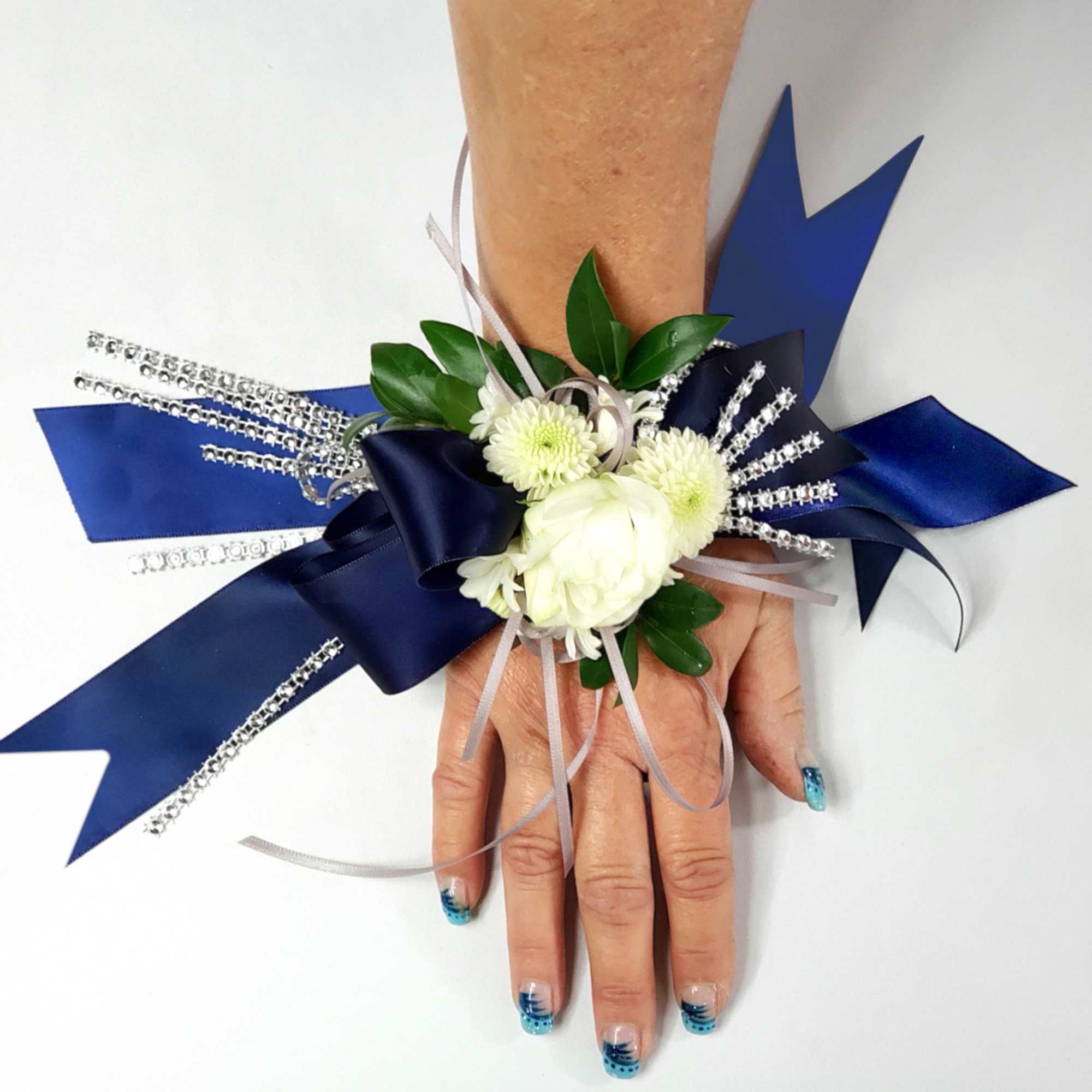 White floral wrist corsage with blue ribbon accents