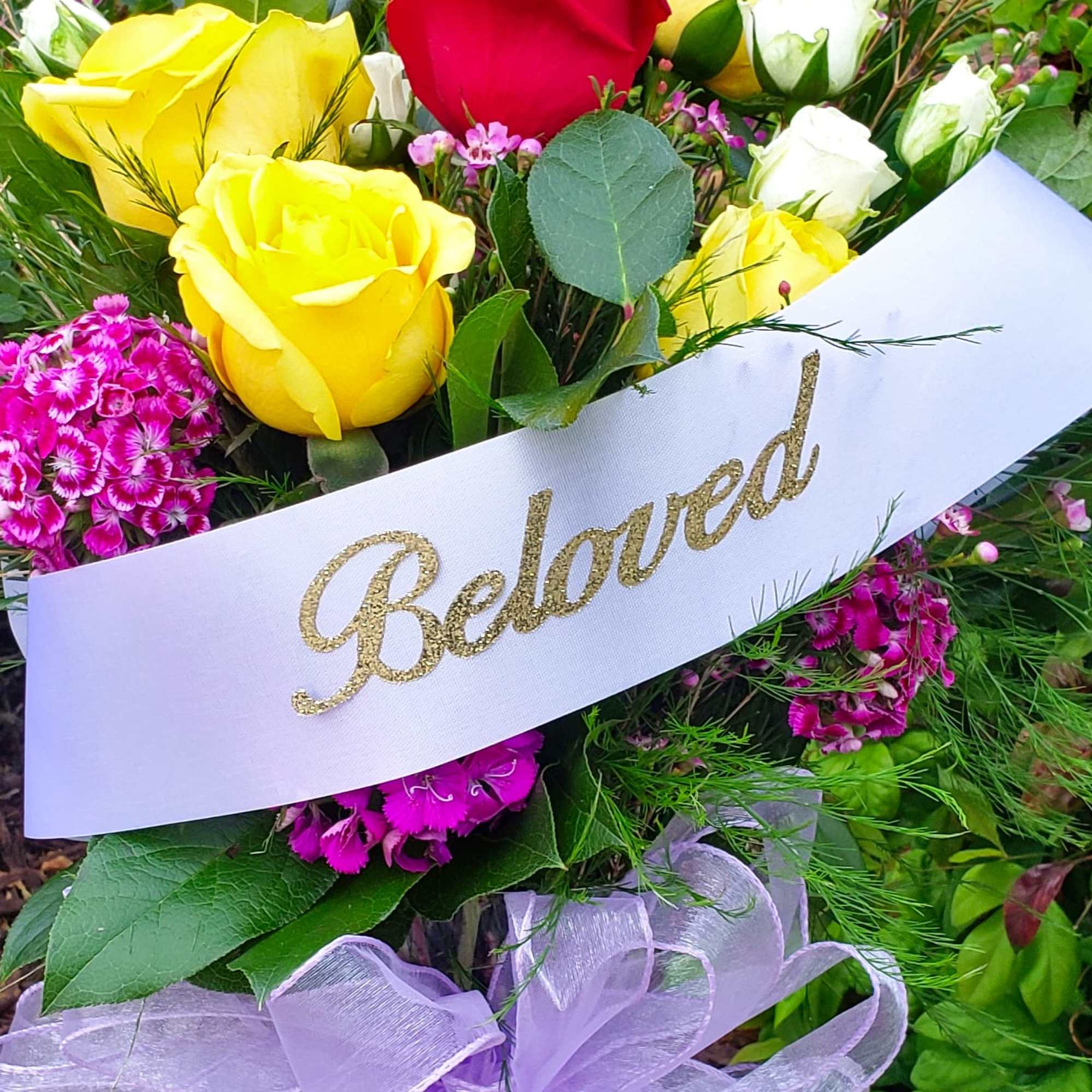 Bouquet of yellow and red roses with pink flowers and a "Beloved" ribbon