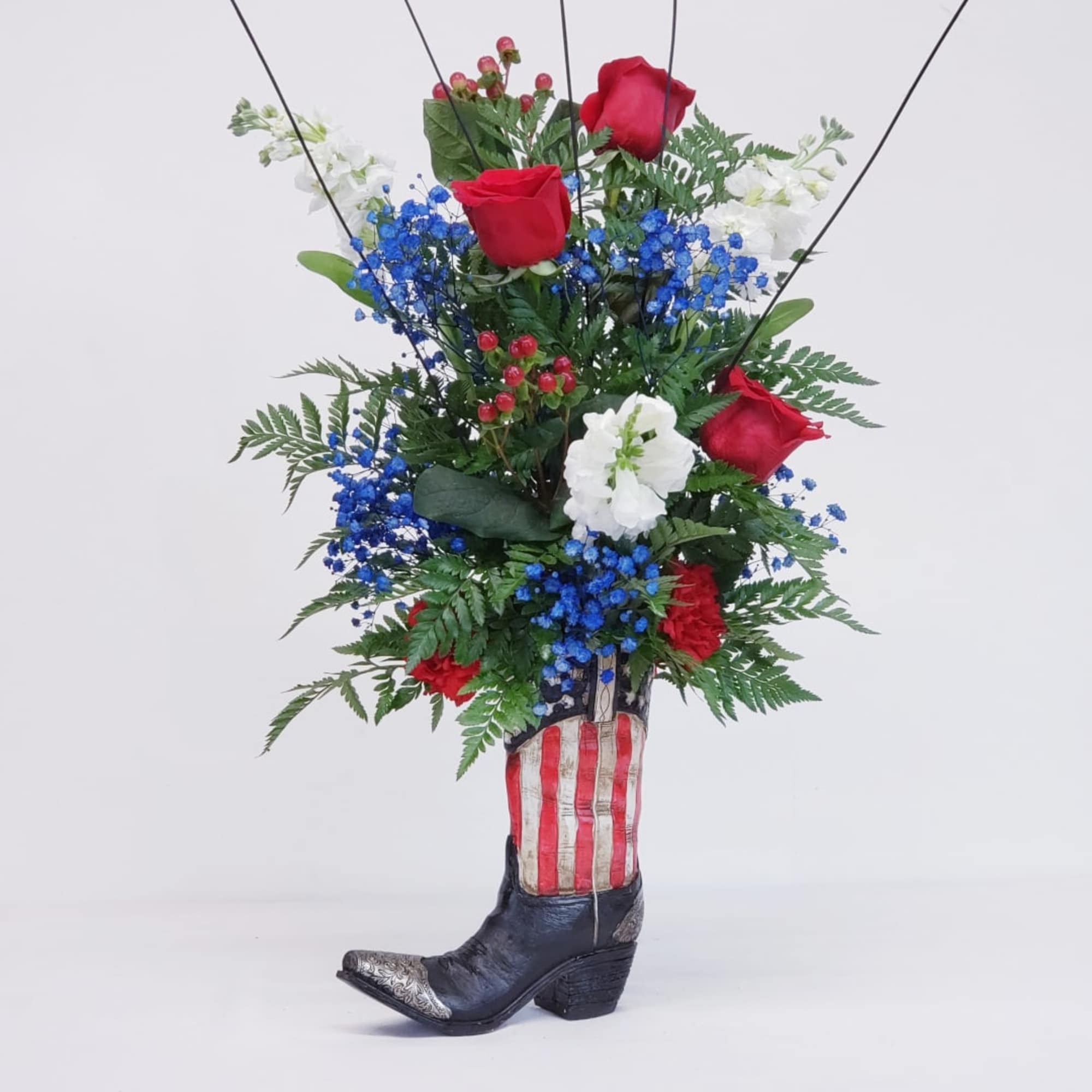 Red roses and blue-white flowers arranged in a cowboy boot vase