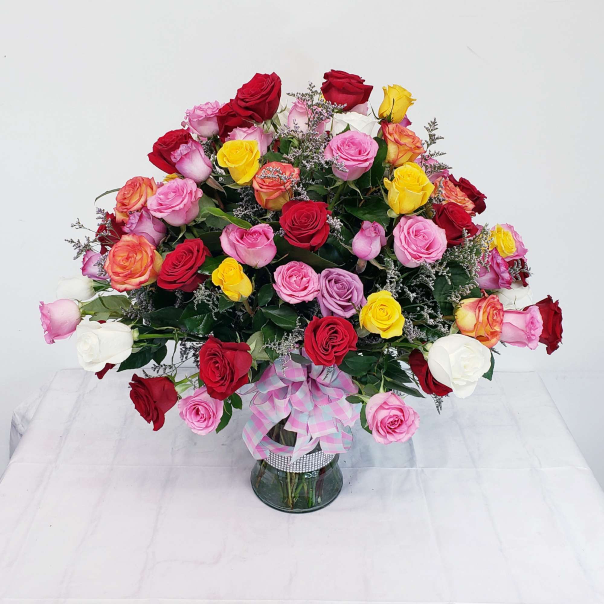 Large bouquet of multicolored roses in a glass vase with a ribbon