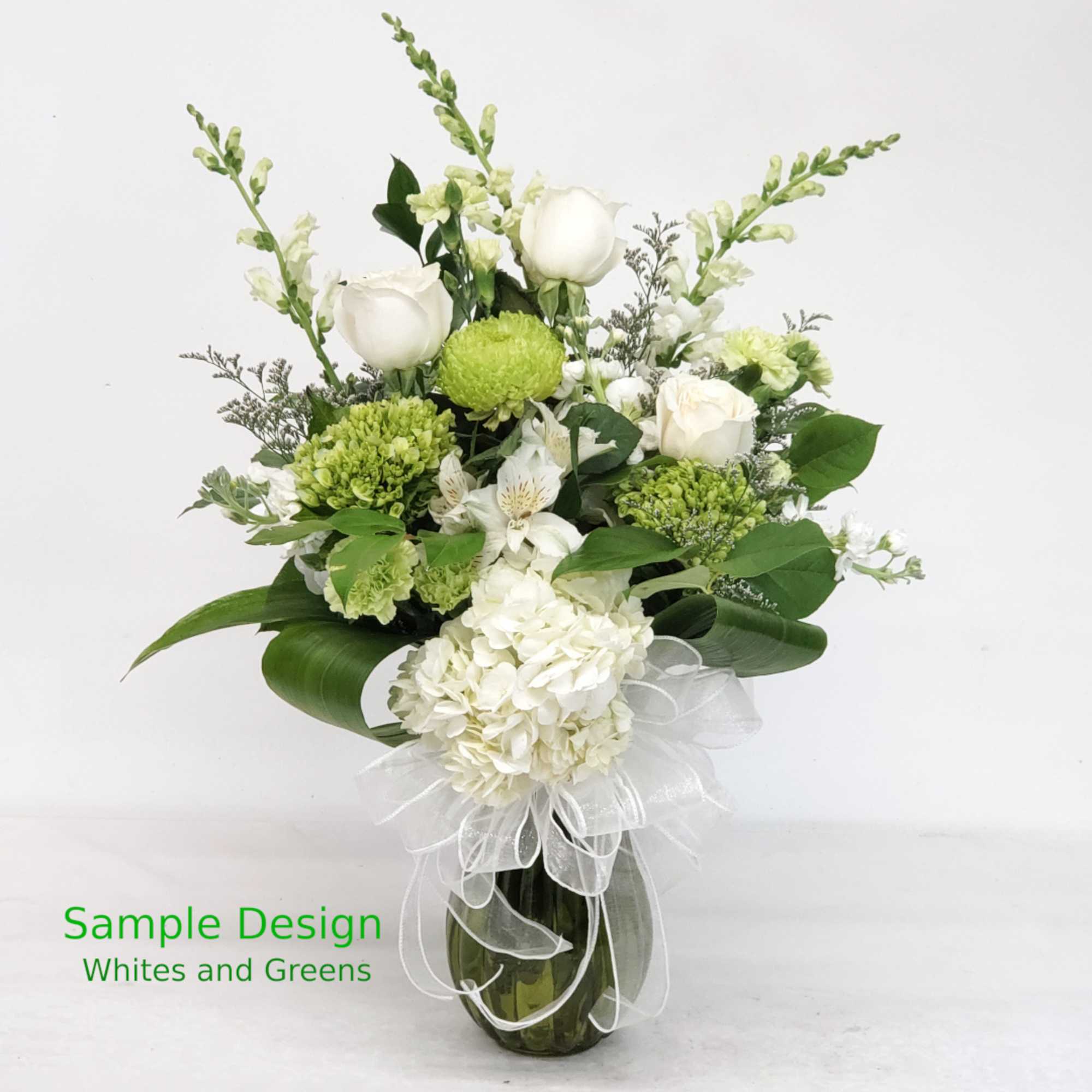 White and green floral arrangement in a glass vase with a white ribbon
