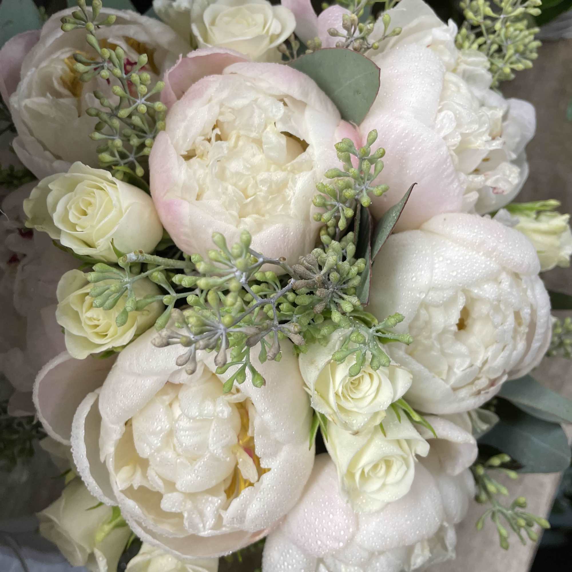 White peonies and cream roses in a bouquet with pale greenery