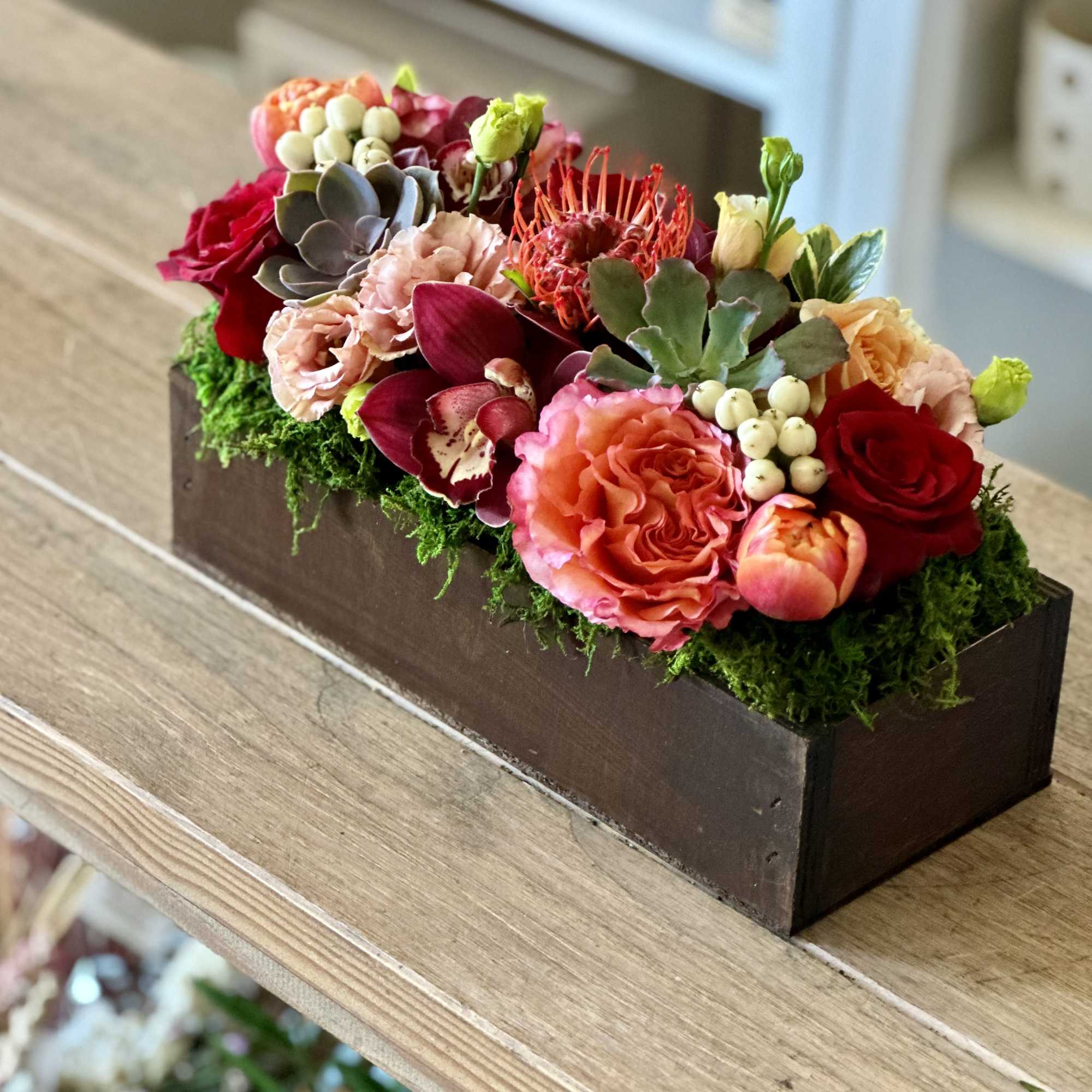 Rectangular floral arrangement in a dark wooden box with pink and red blooms