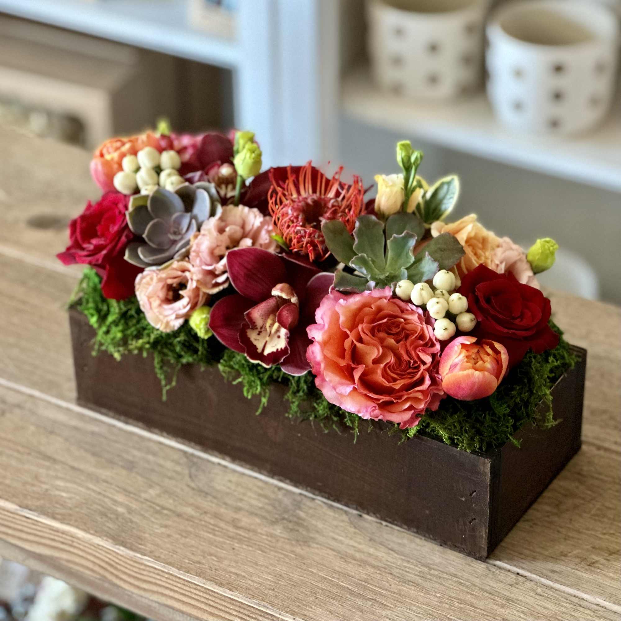 Mixed floral arrangement in a rectangular wooden box with roses and orchids