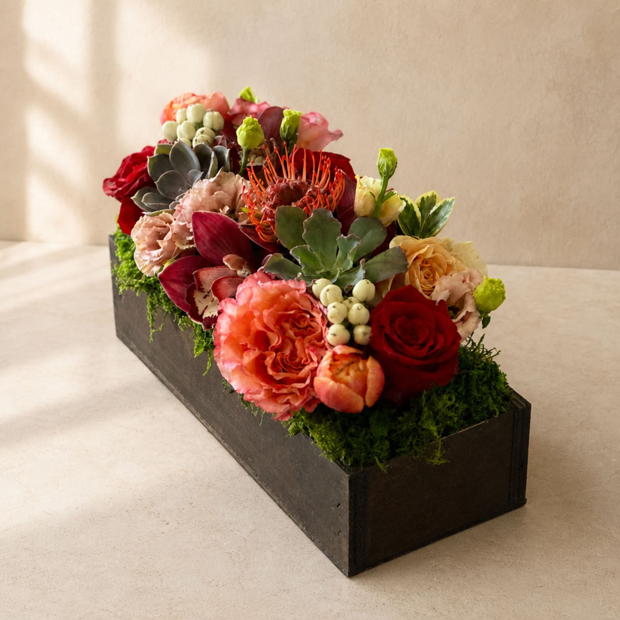 Rectangular floral arrangement with red, pink, and peach blooms in a black box