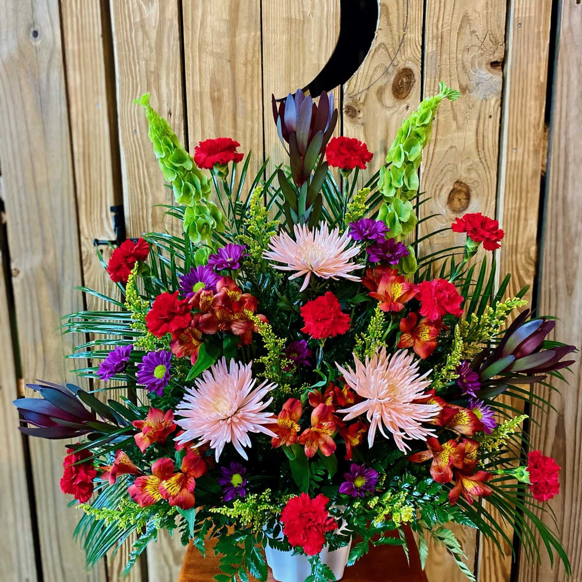 Colorful floral arrangement with red, purple, and pale pink blooms in a white container