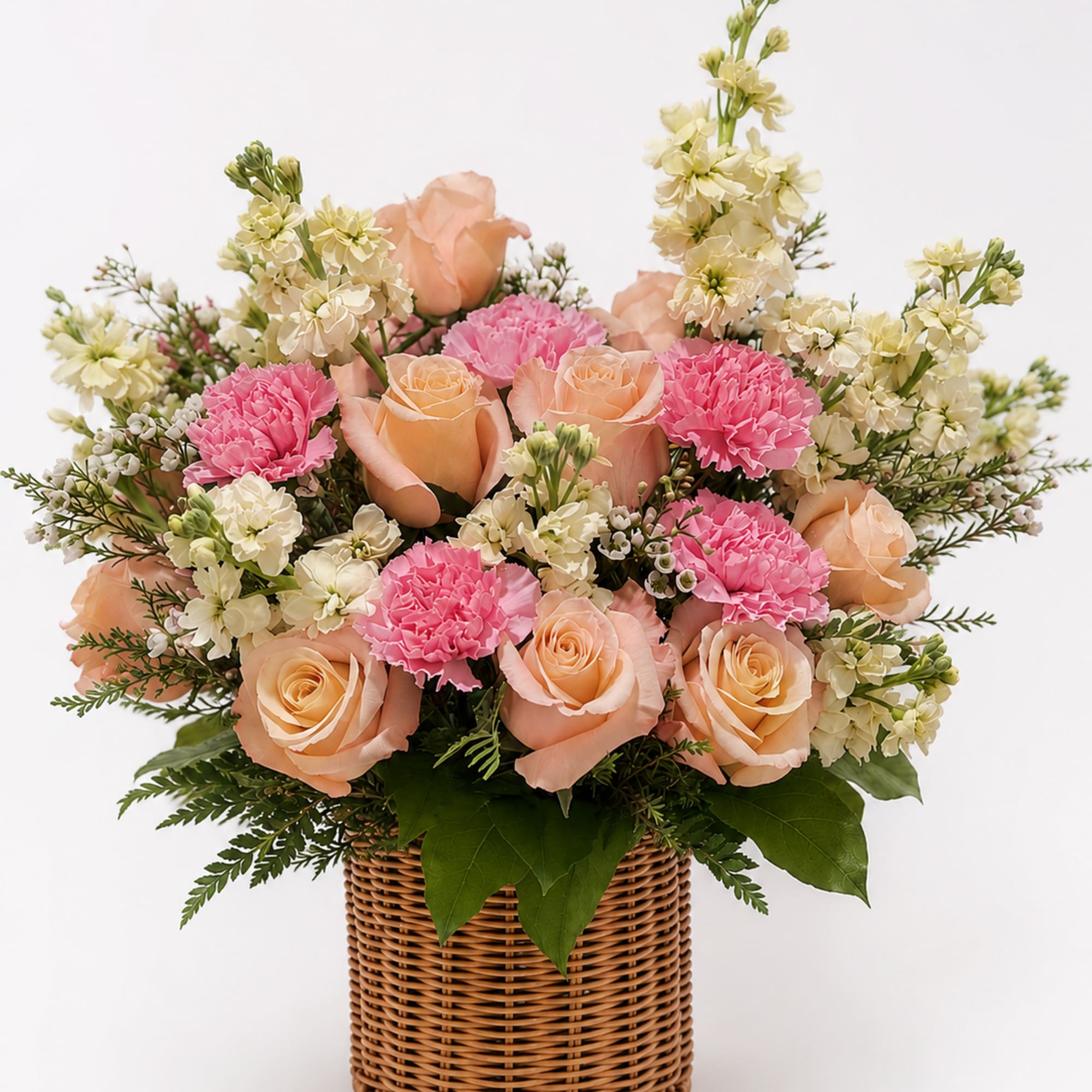 A charming basket arrangement featuring elegant peach roses, soft pink carnations, creamy