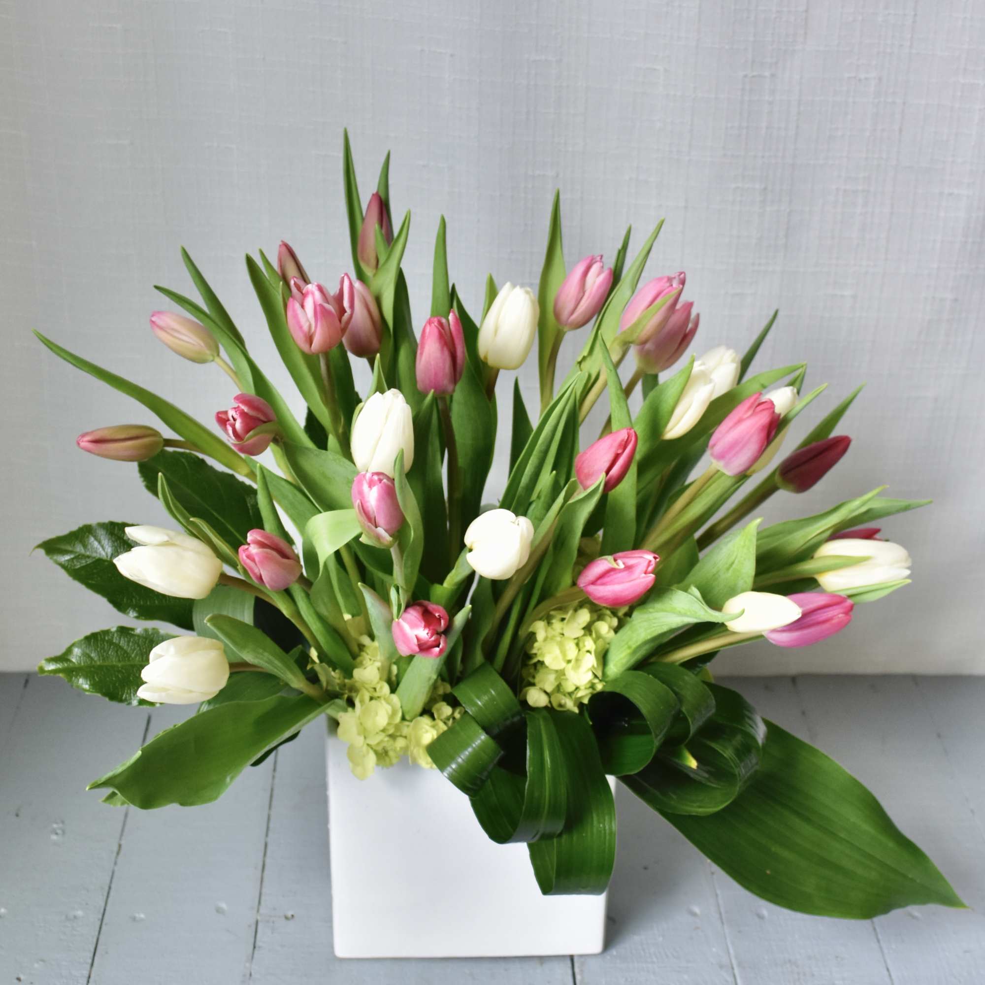 Pink and white tulips with green accents arranged in a white square vase