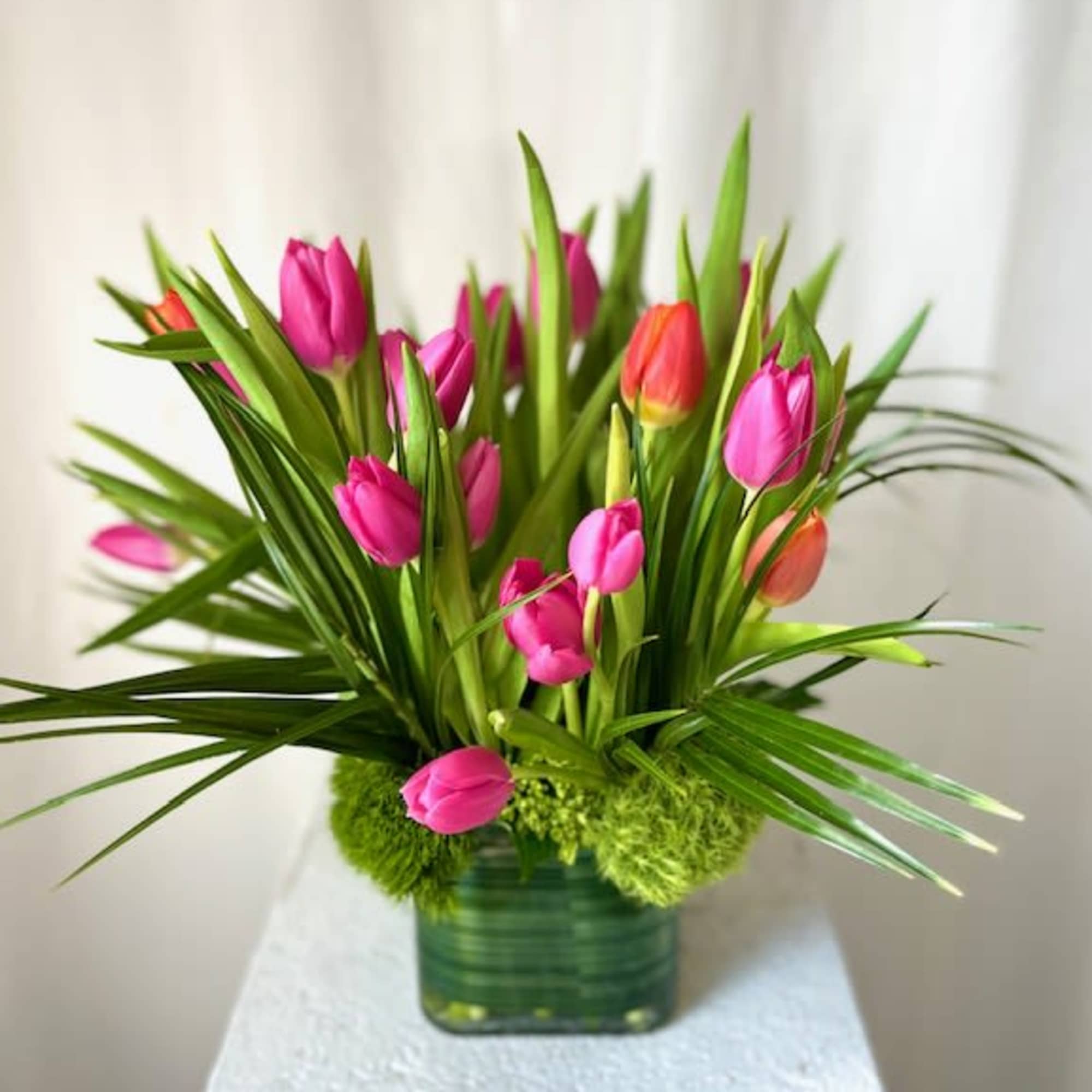 Pink and orange tulips with tall green foliage in a square glass vase
