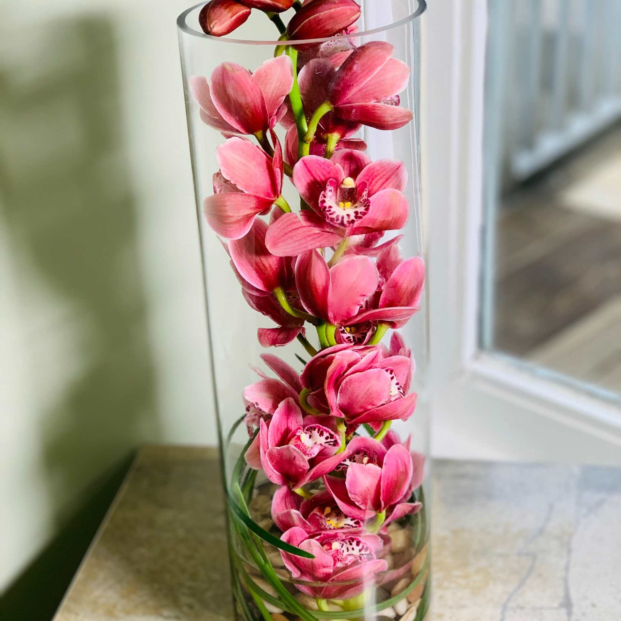 Pink orchid blooms arranged in a tall clear glass cylinder