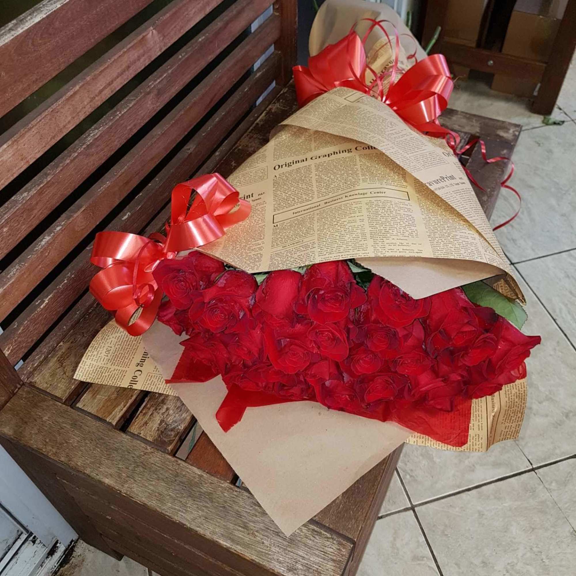 Bouquet of red roses wrapped in newspaper-style paper with red ribbon bows
