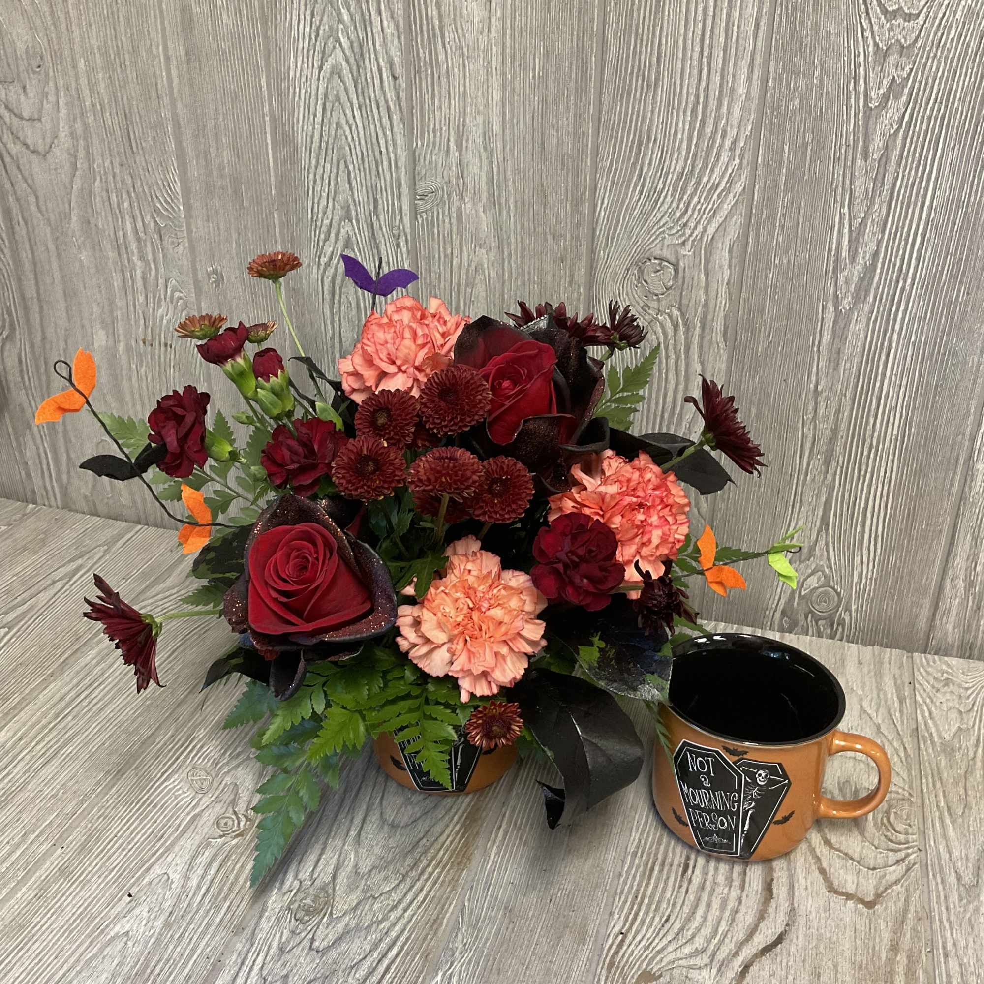 Halloween floral arrangement in an orange container with a matching mug beside it