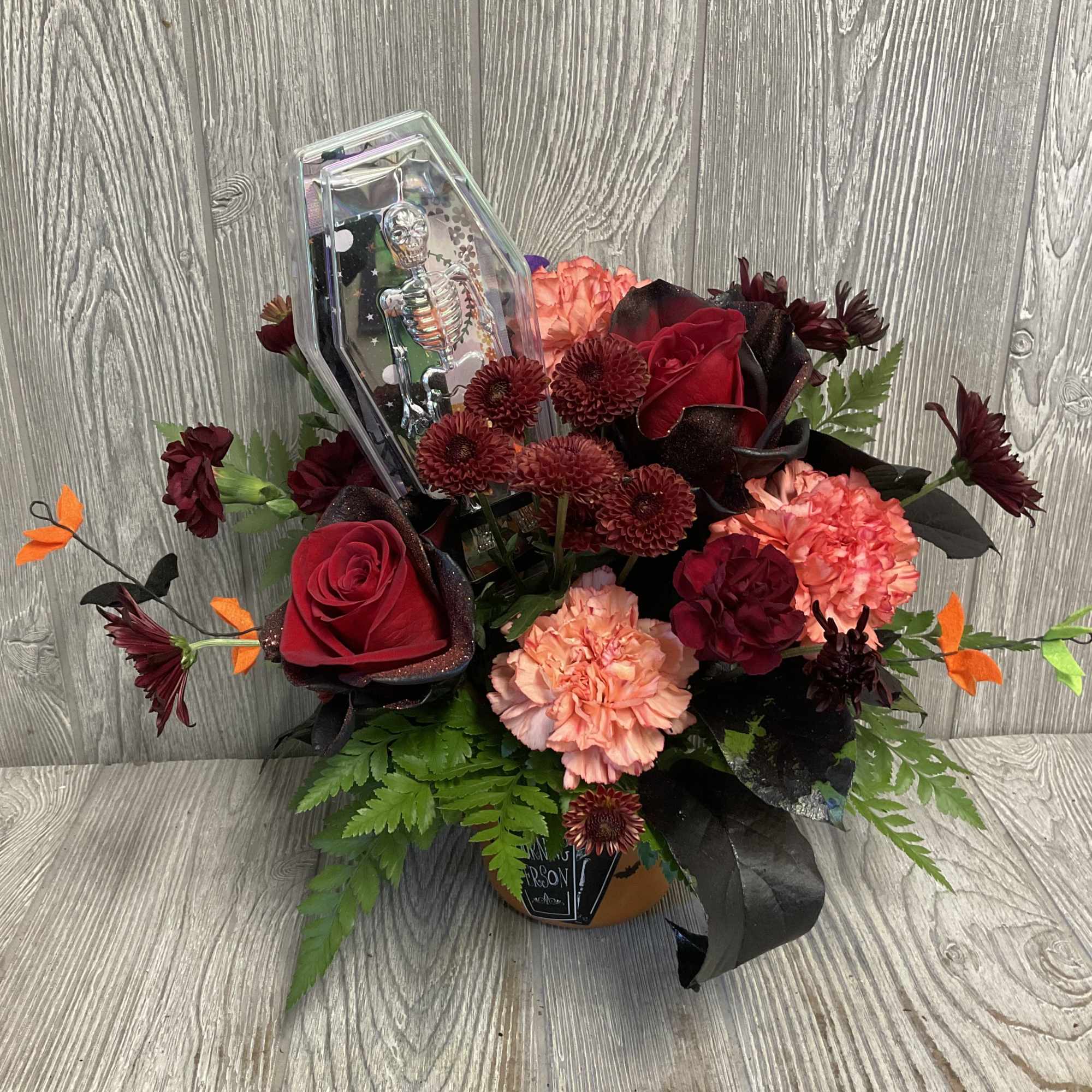 Bouquet of red roses and peach carnations with a clear coffin-shaped ornament