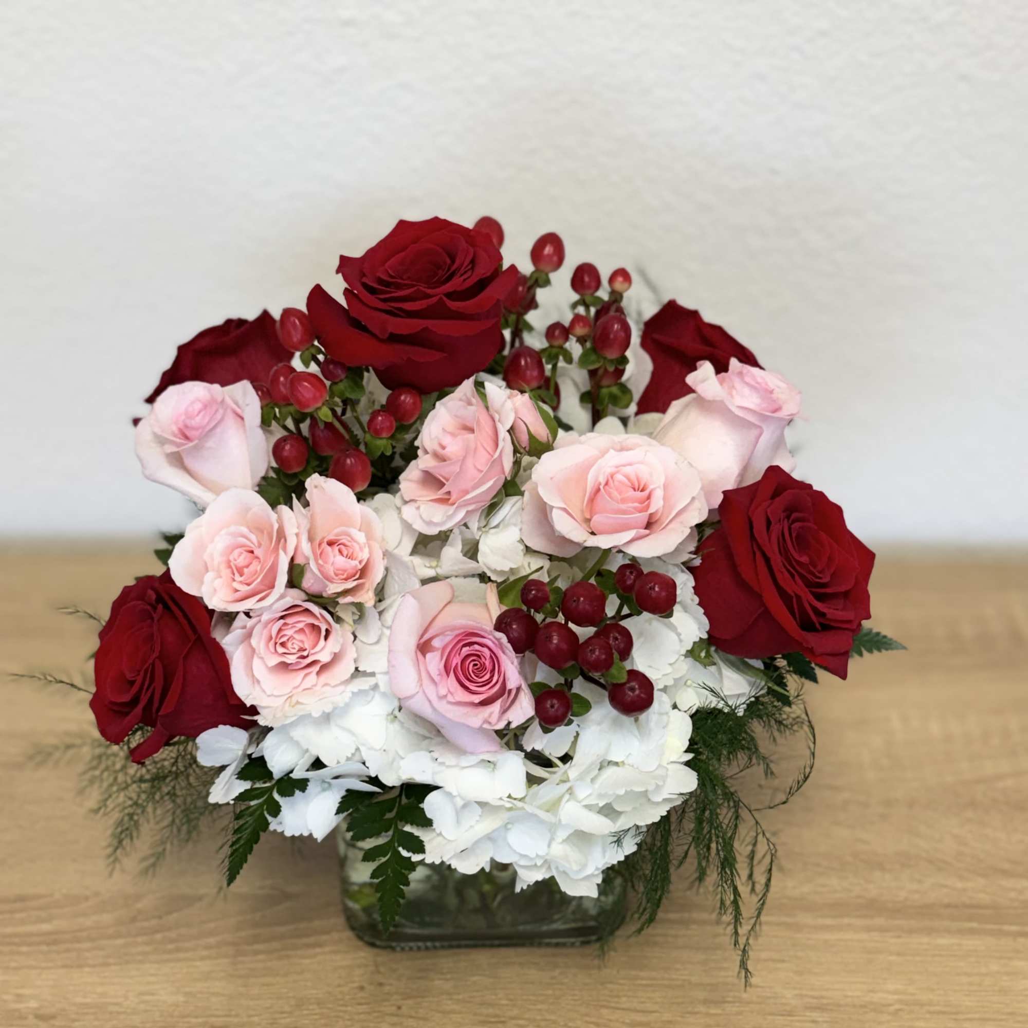 Red and pink roses arranged in a glass vase with white flowers