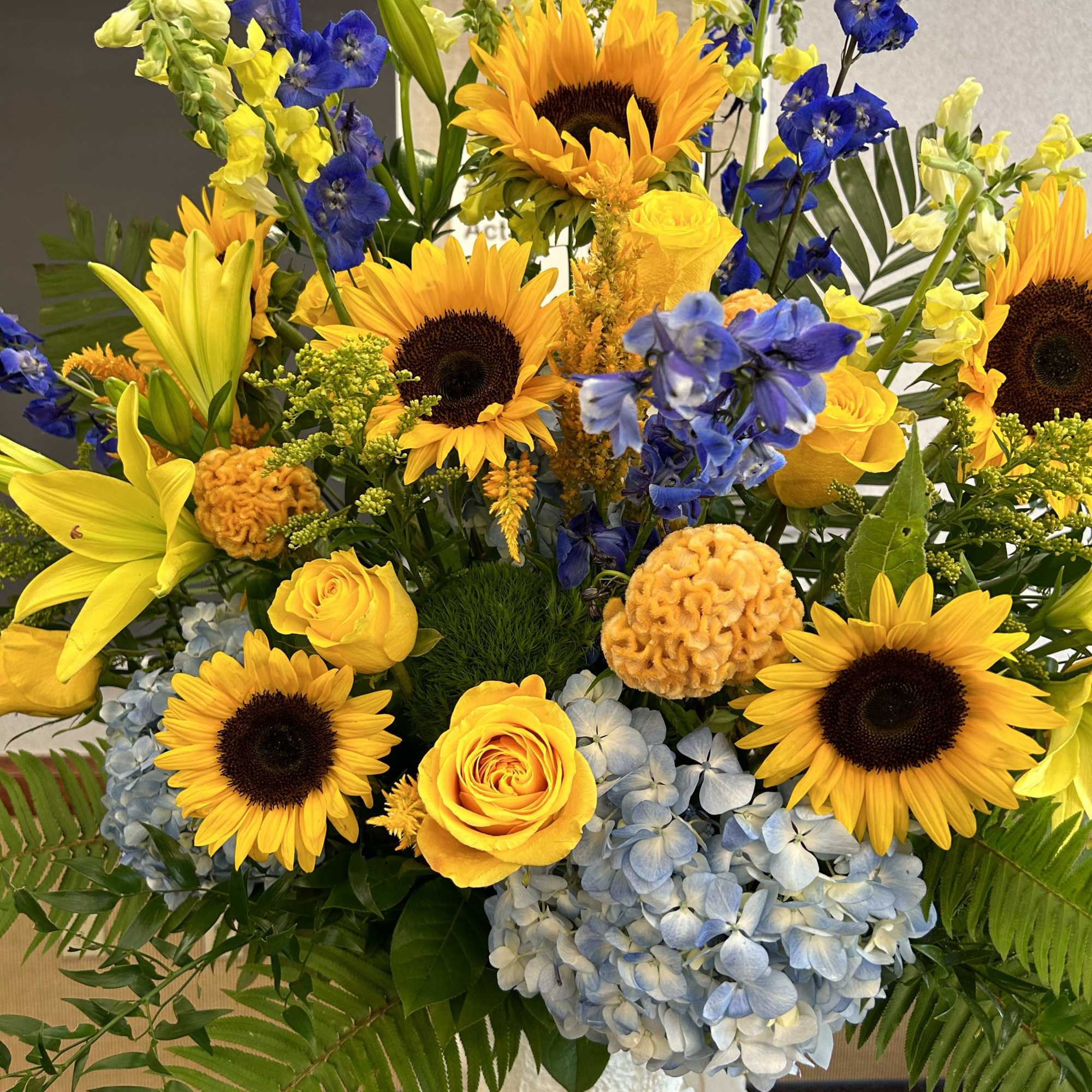 Bright bouquet of sunflowers, yellow roses, blue flowers, and hydrangeas in a white vase