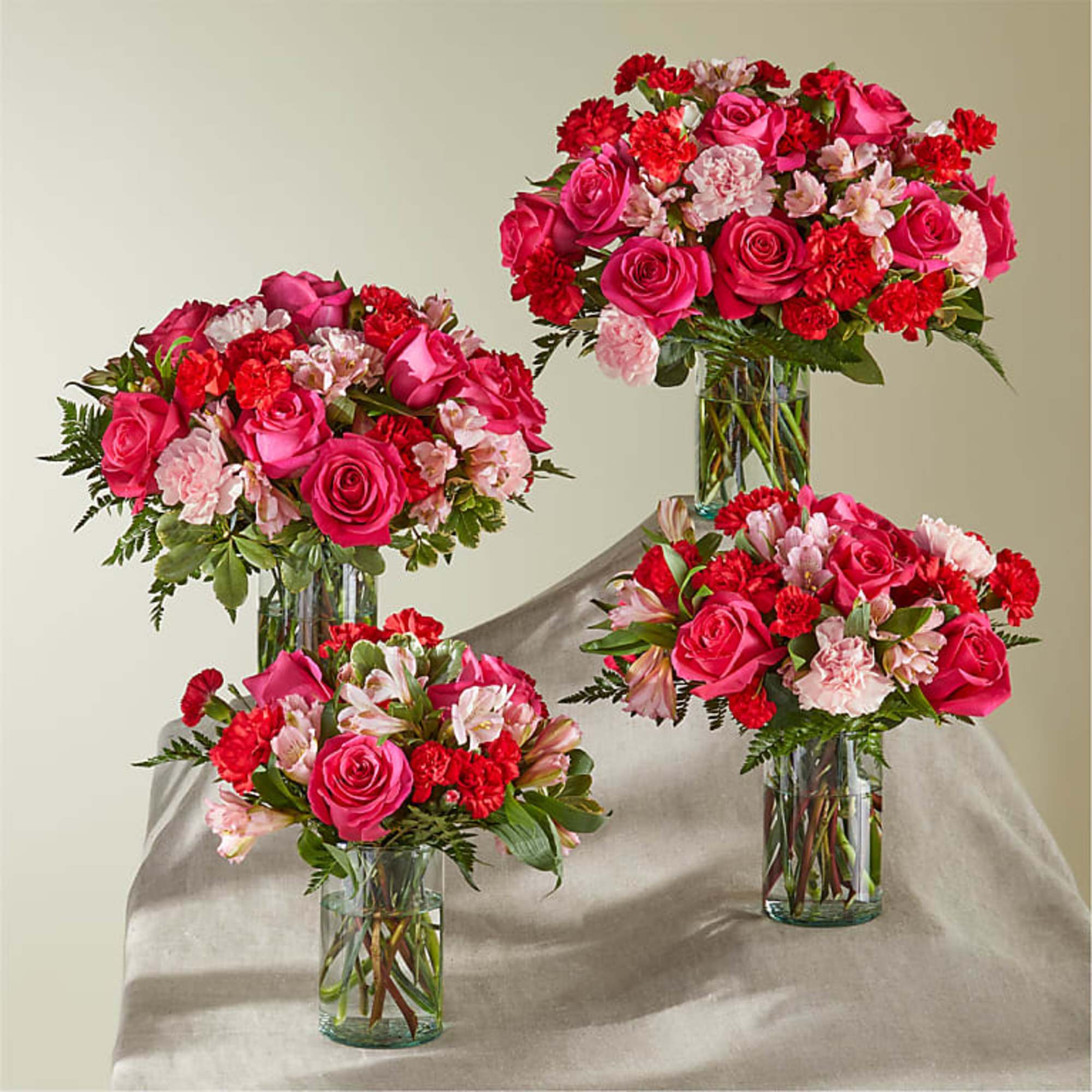 Four pink and red floral arrangements in clear glass vases