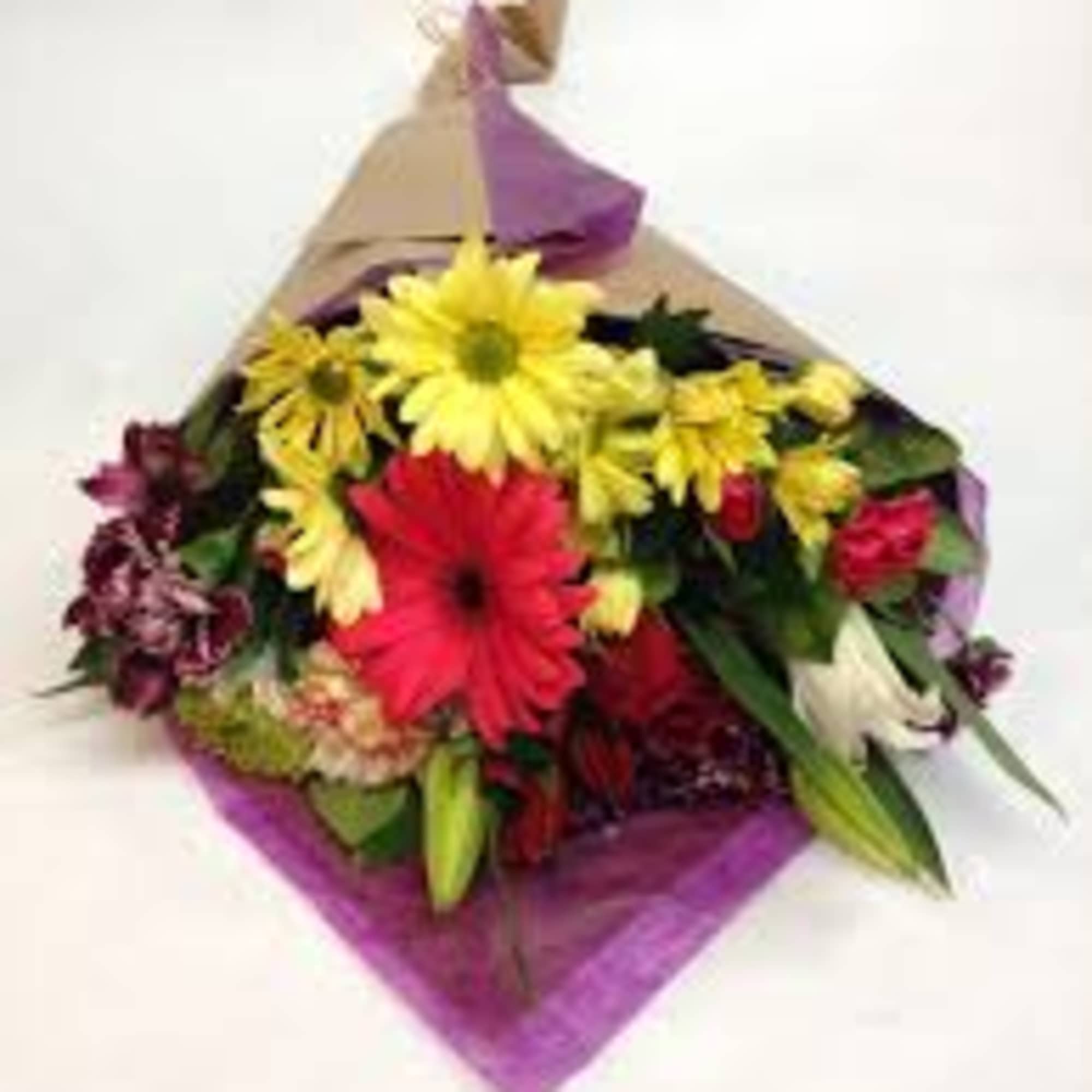 Mixed bouquet of yellow daisies, red gerbera and assorted flowers wrapped in kraft paper with purple tissue.