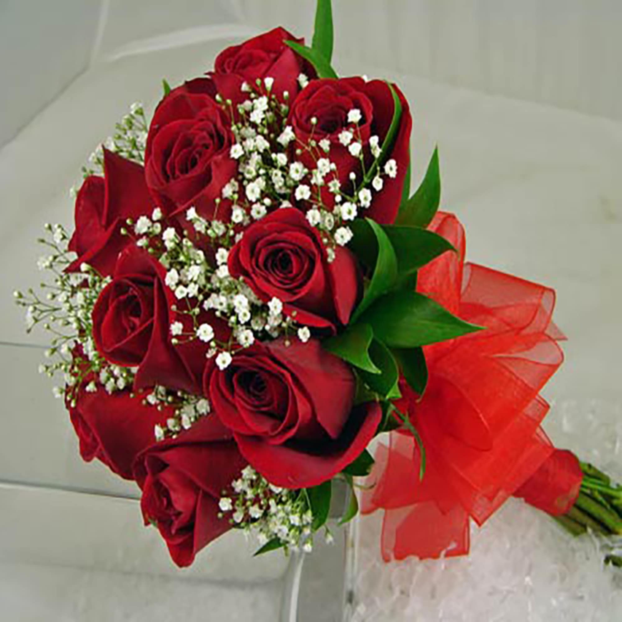 Hand-tied bouquet of red roses with small white filler flowers and a red ribbon bow