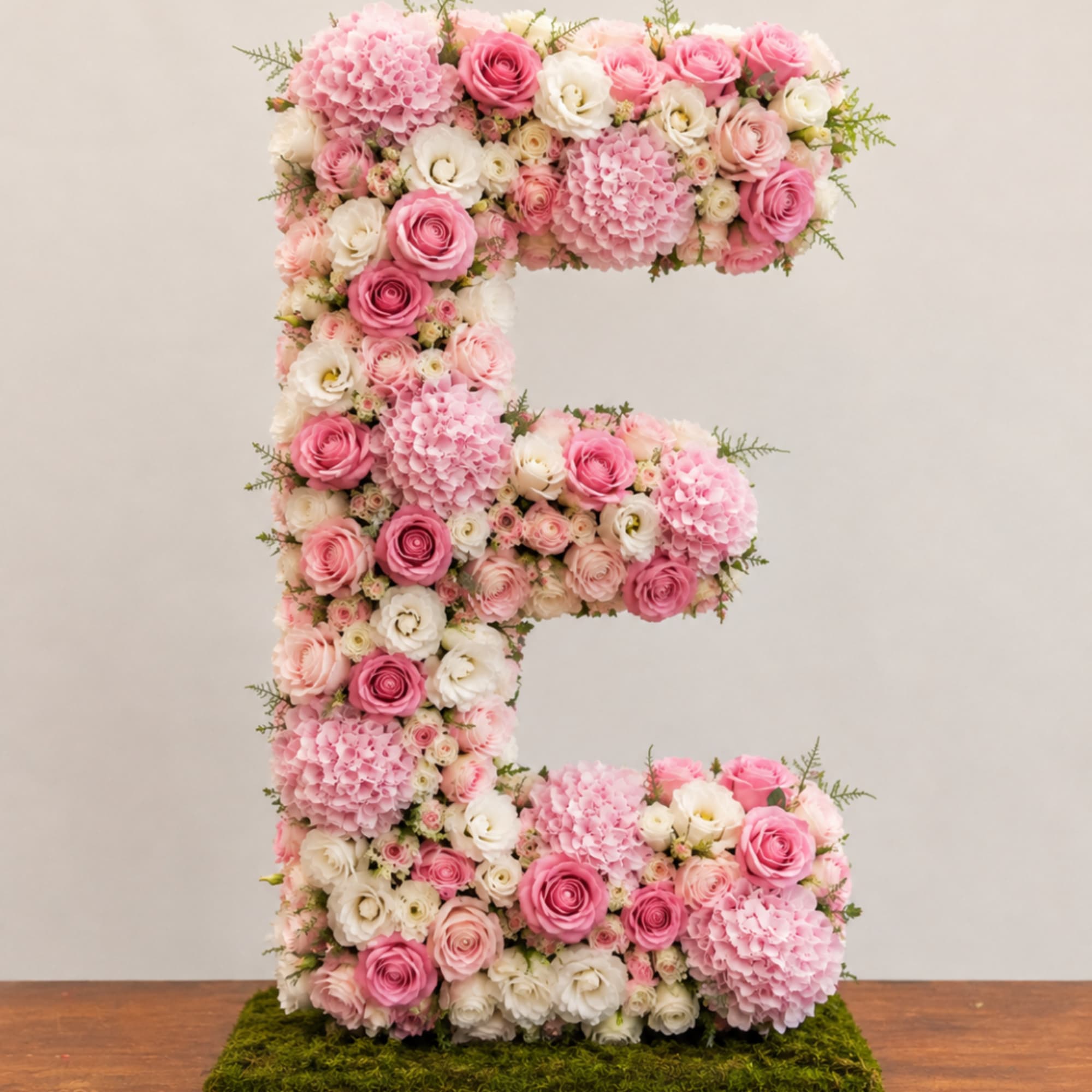 Pink and white floral letter E arrangement on a moss base