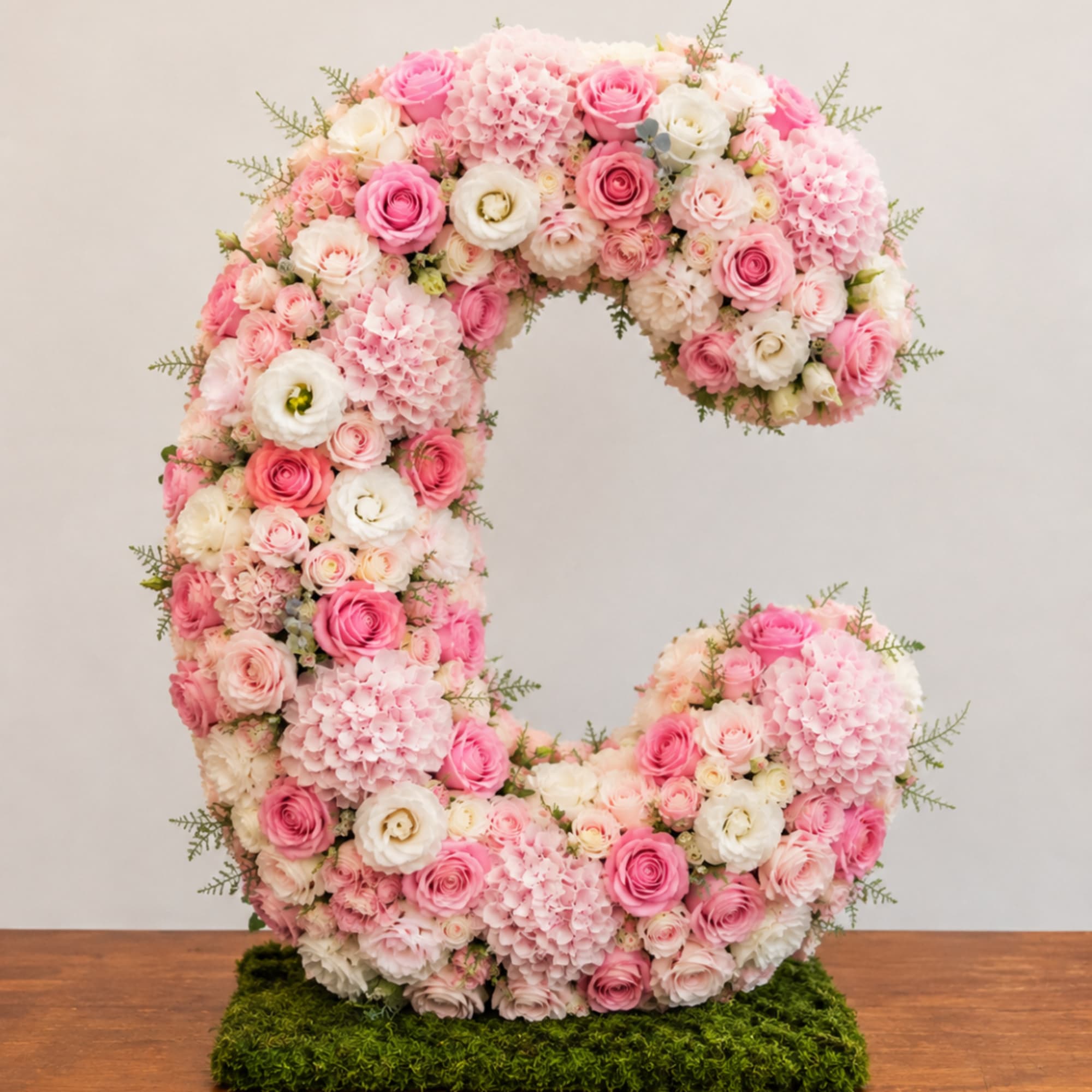 Large floral letter C covered in pink and white blooms on a moss base