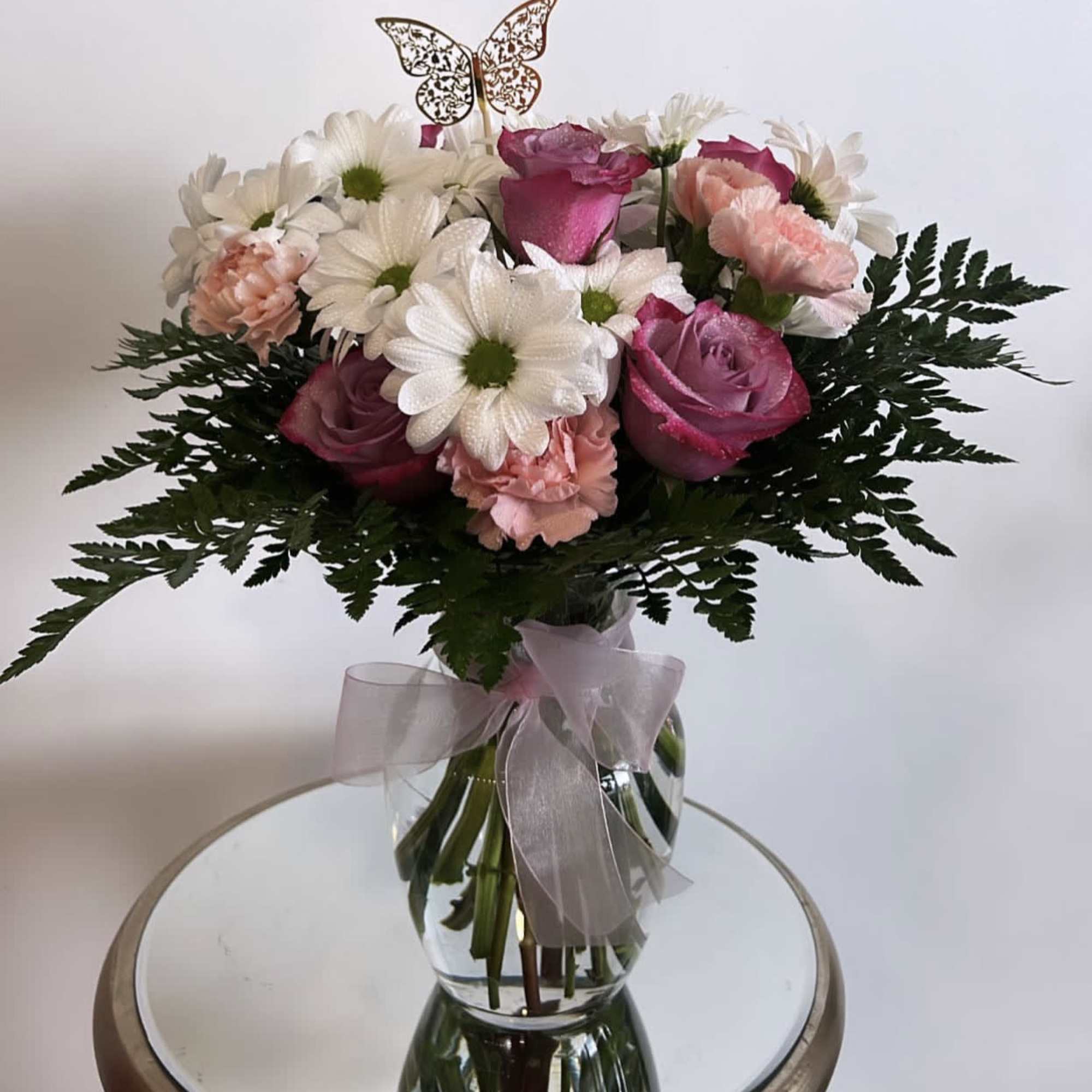 Pink roses and white daisies in a clear glass vase with a ribbon