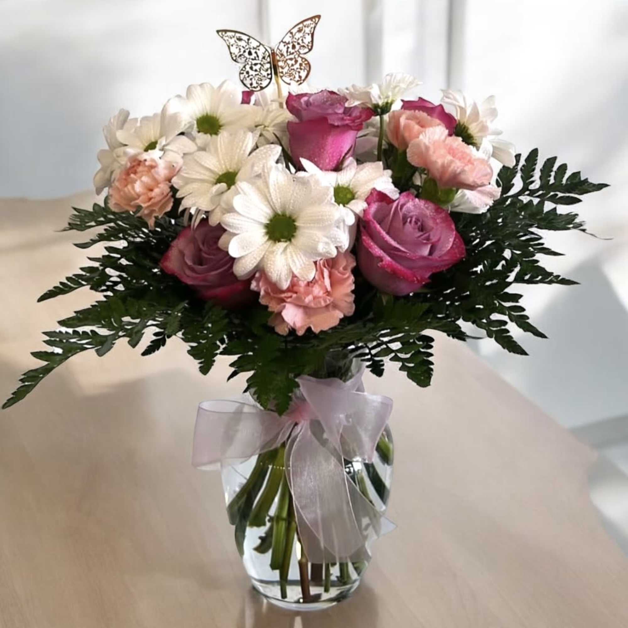 Pink roses and white daisies in a glass vase with a ribbon