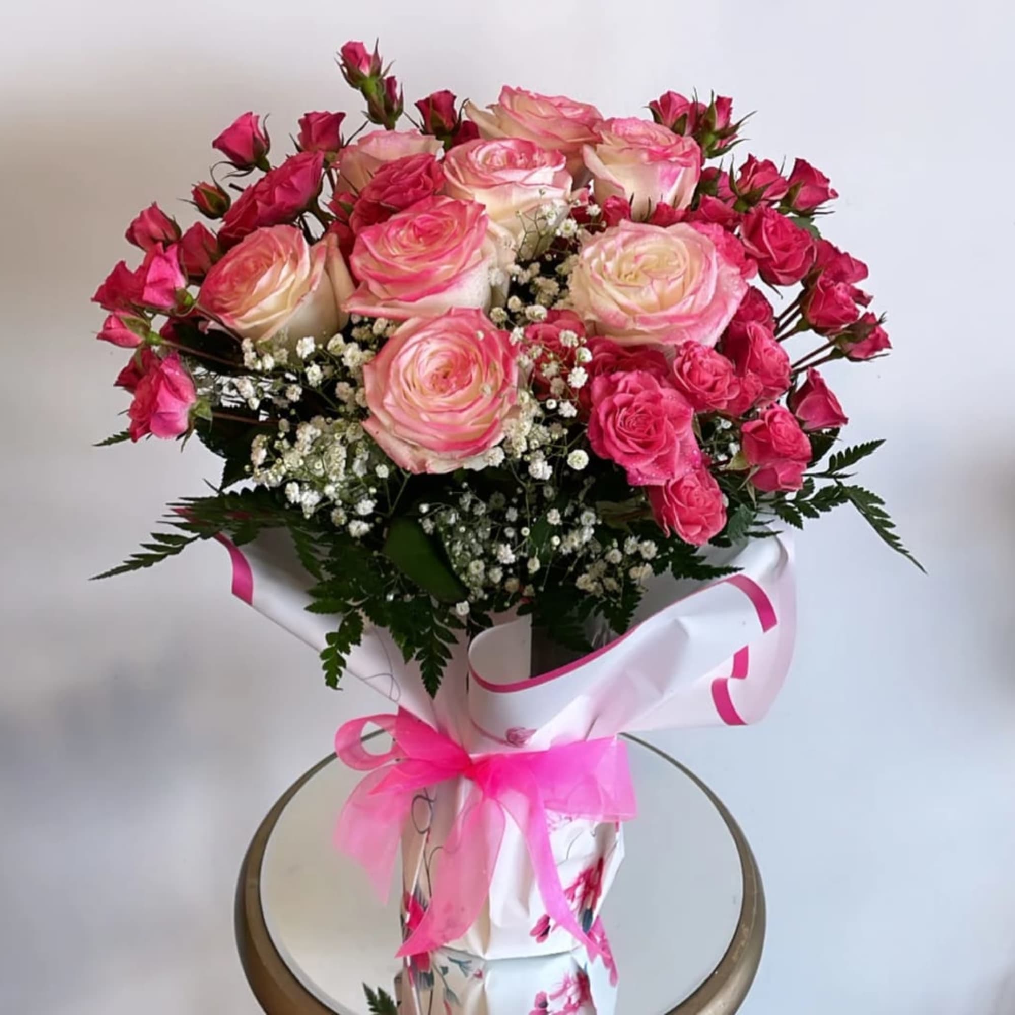 Pink and cream roses arranged in a wrapped bouquet with a pink ribbon