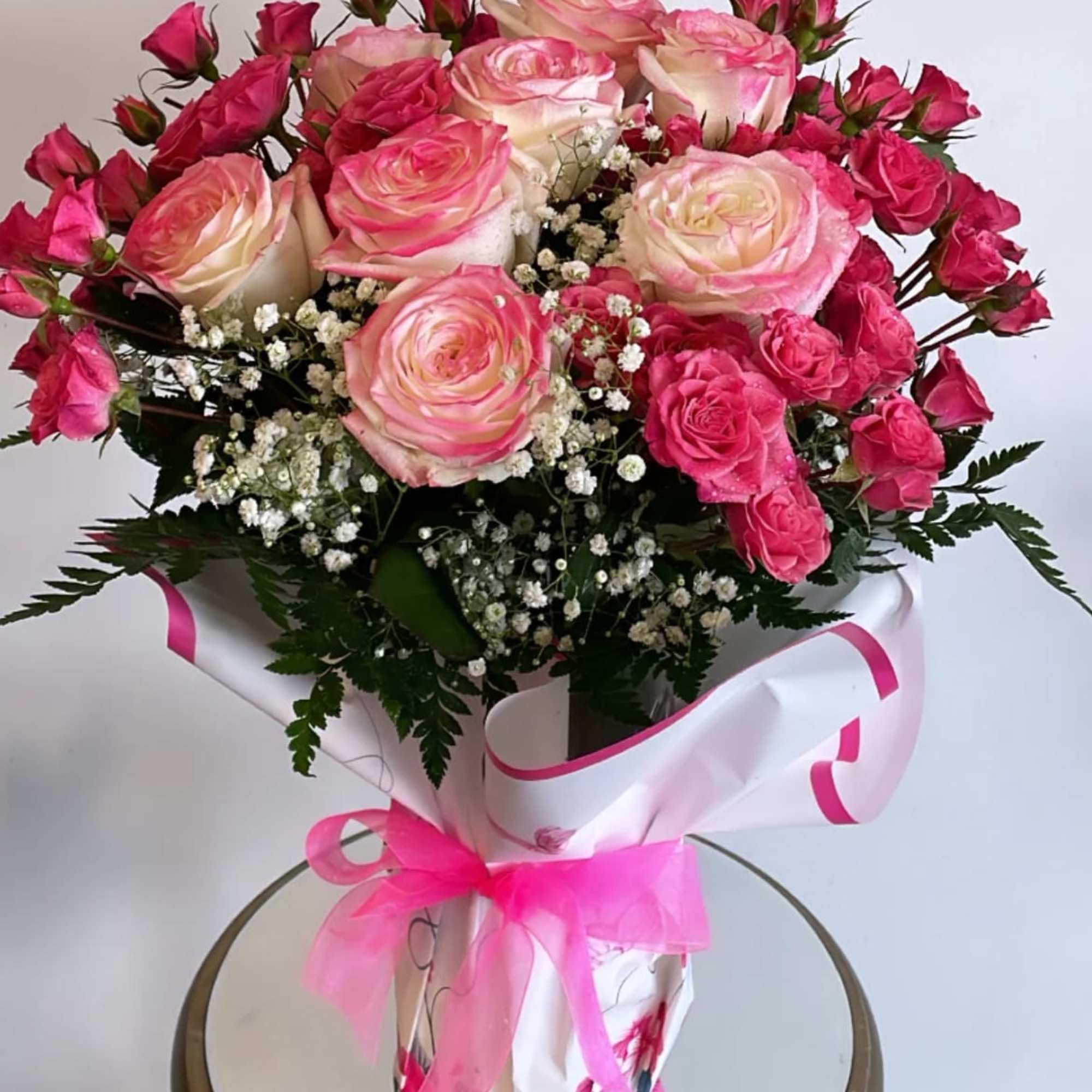 Pink and cream rose bouquet wrapped in white paper with a pink ribbon