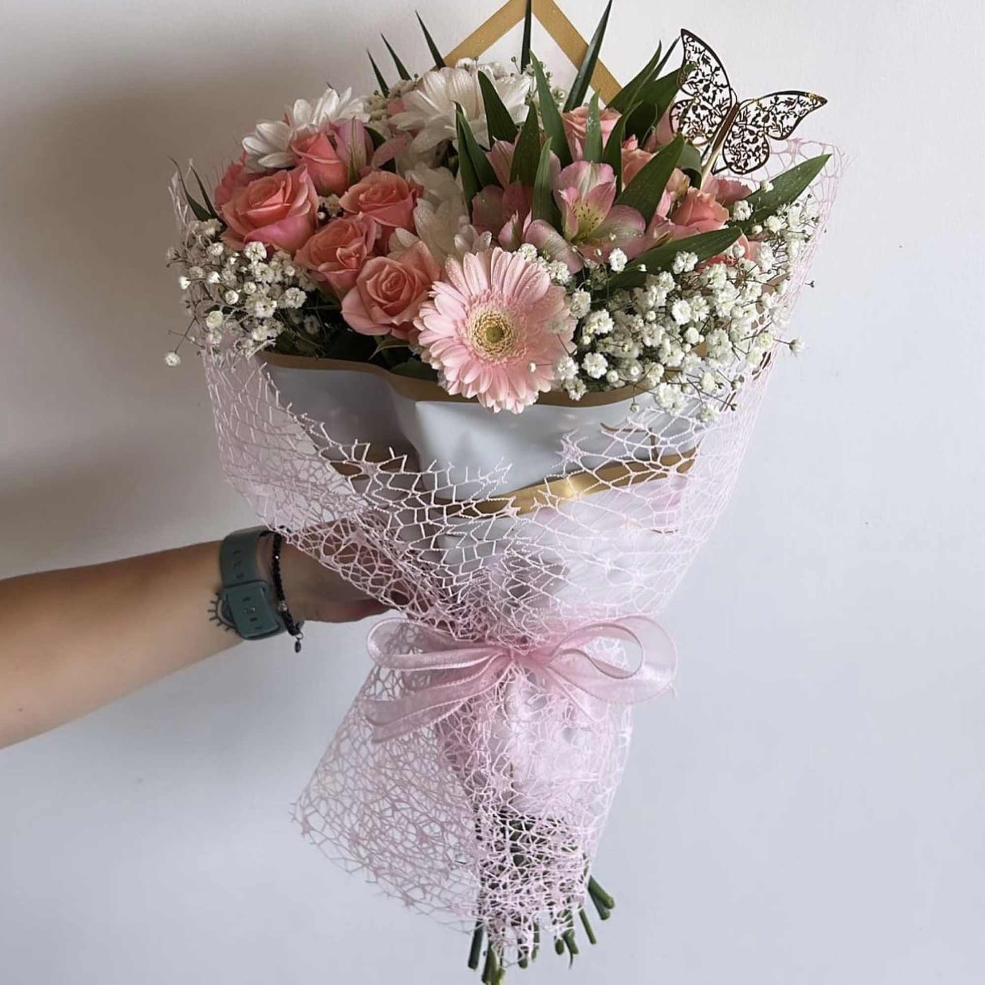 Handheld bouquet of pink roses, gerbera daisies, and white filler flowers wrapped in pink mesh
