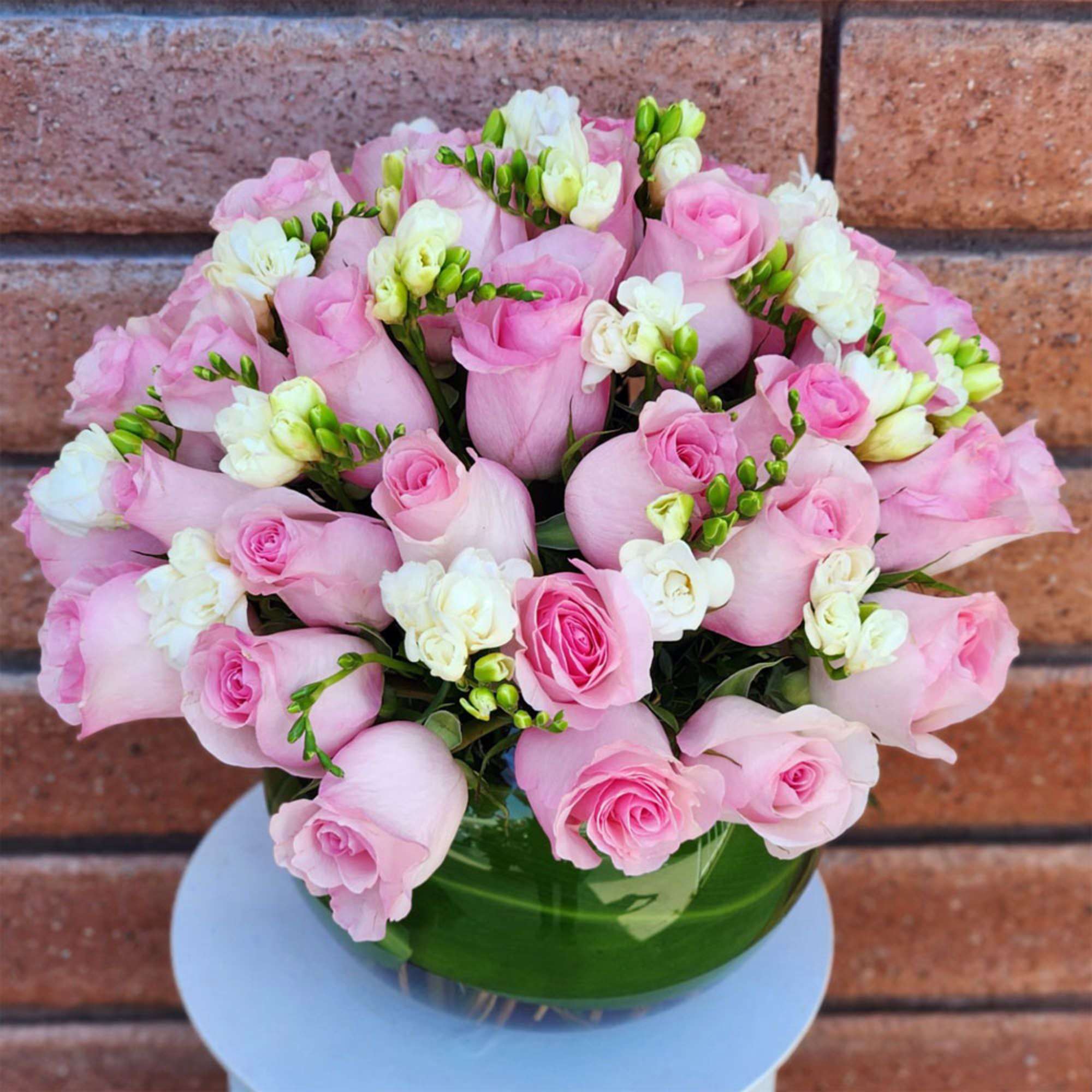 Pink roses and white freesia arranged in a green glass vase