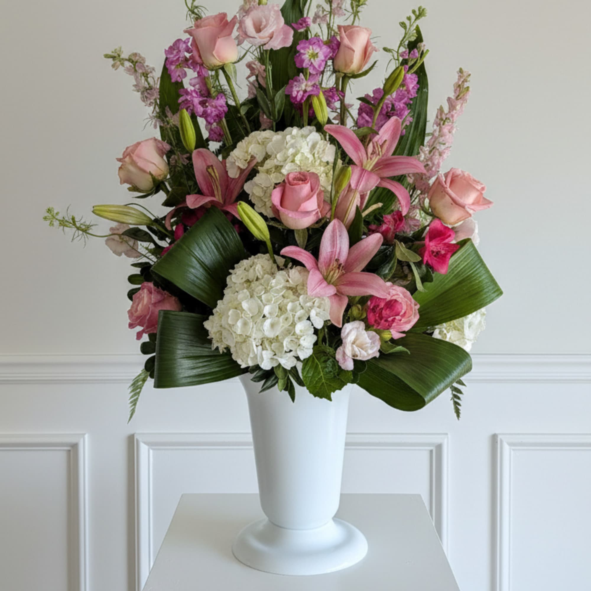 This elegant arrangement features soft blush and pink blooms including roses, lilies