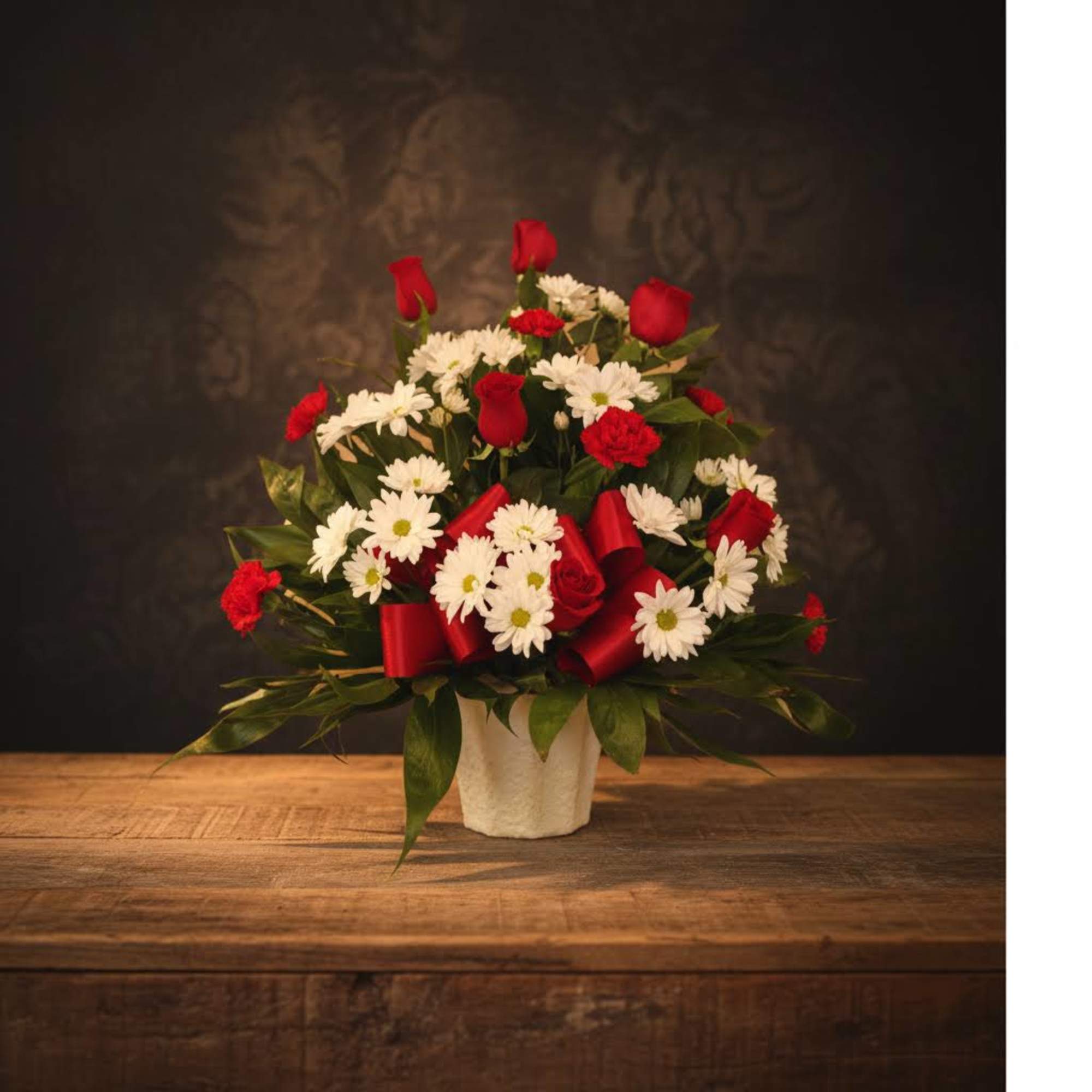 Red roses and white daisies arranged in a white vase