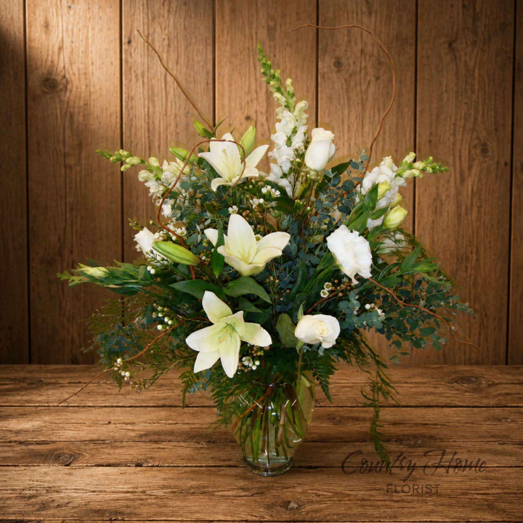 White lilies and roses arranged in a clear glass vase
