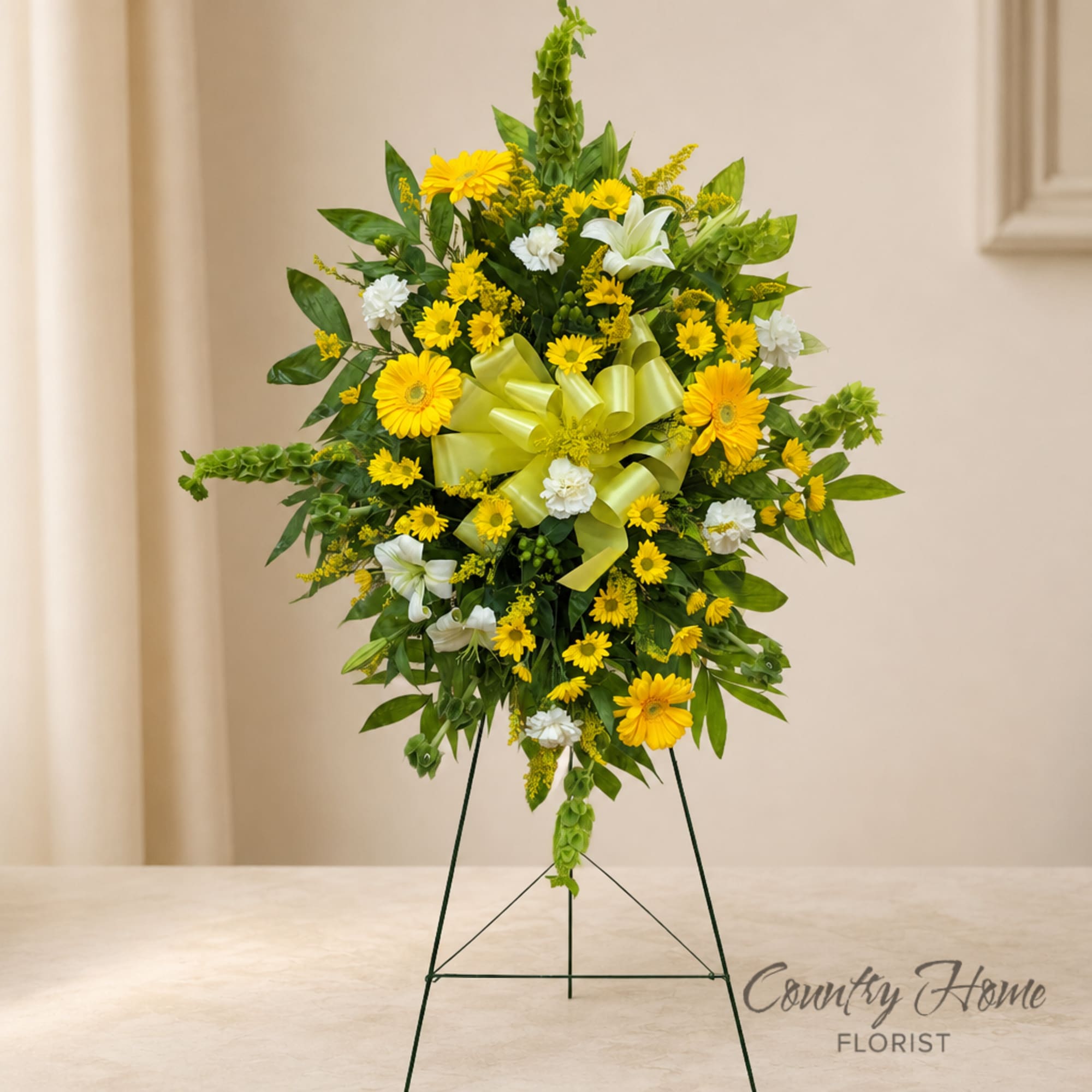 Yellow and white floral standing wreath on an easel with a green ribbon bow