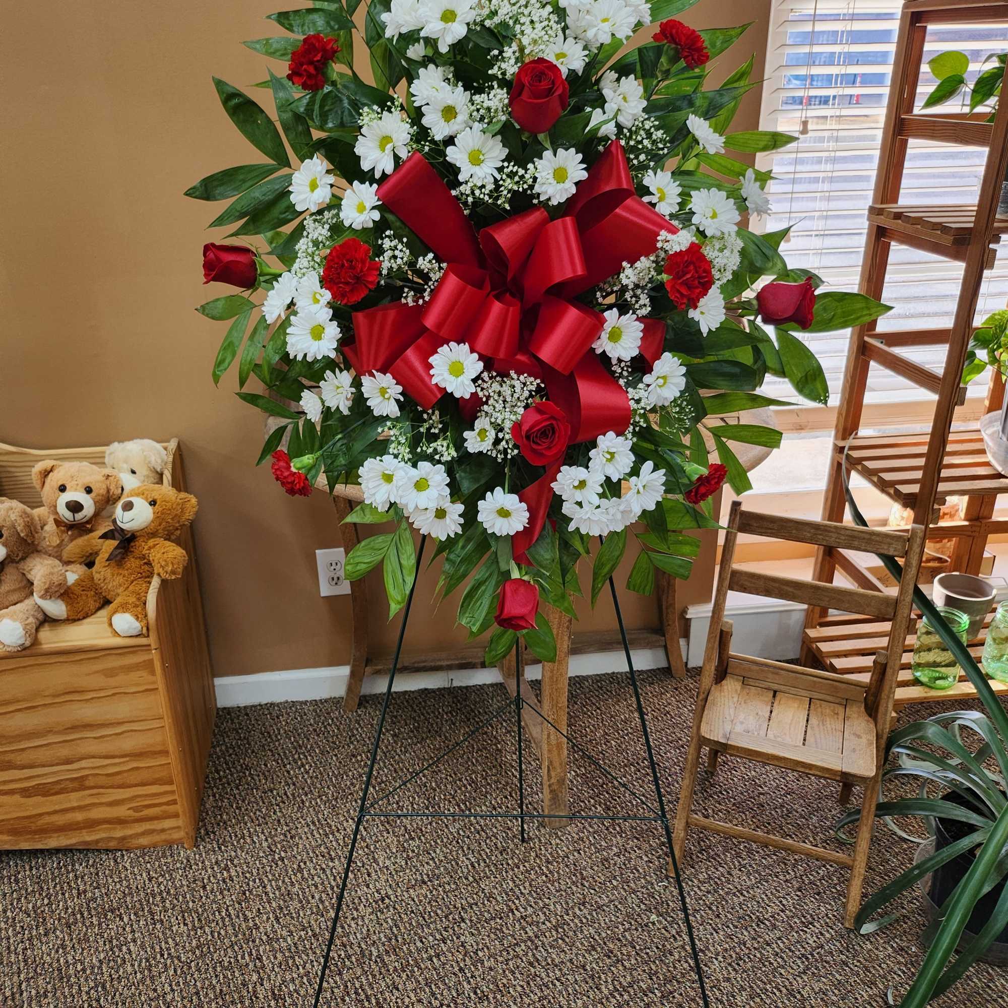 Standing floral spray with red roses, white daisies, and a large red bow
