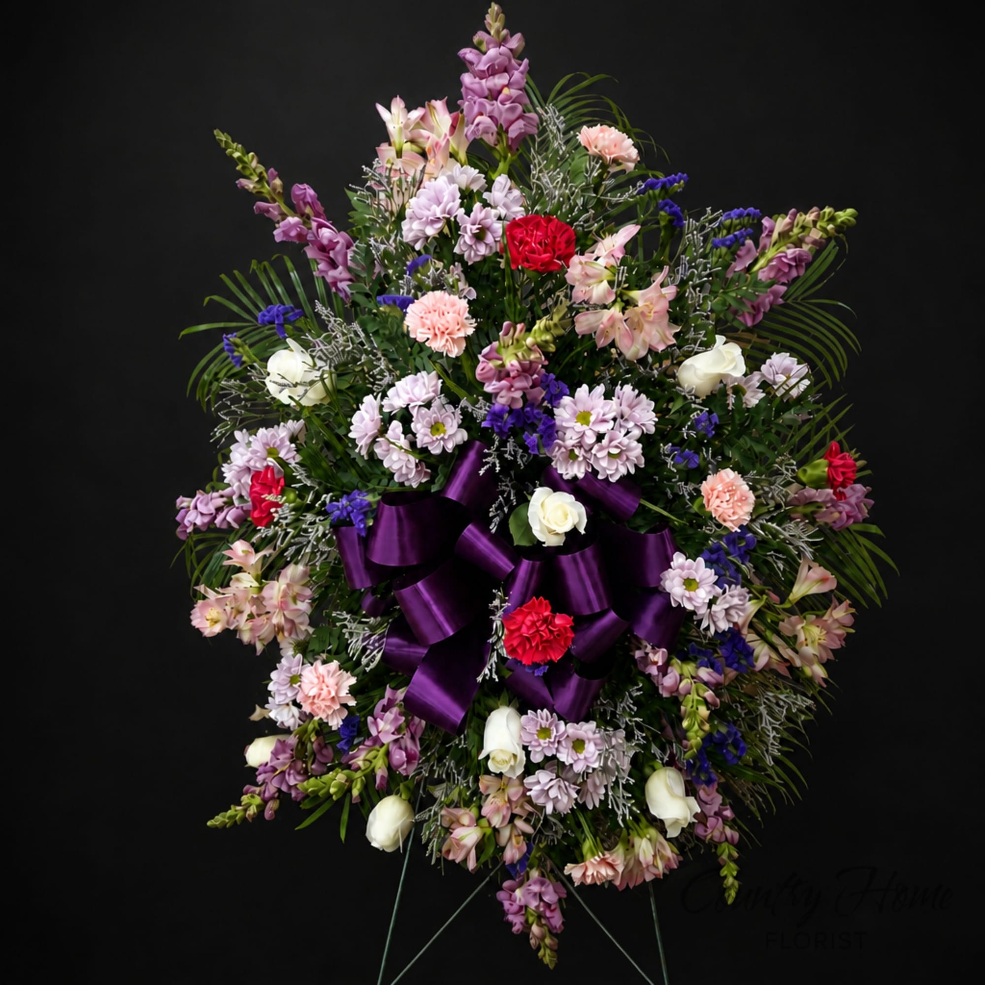 Large purple and pink funeral wreath with ribbon on a stand