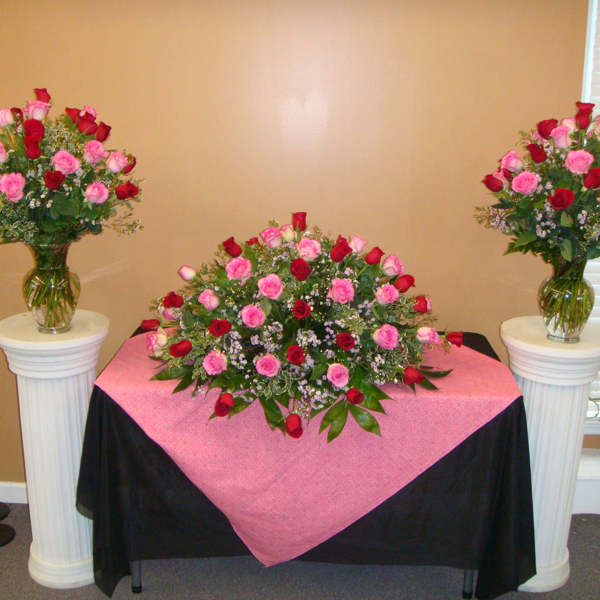 Three rose arrangements in glass vases on pedestals and a table