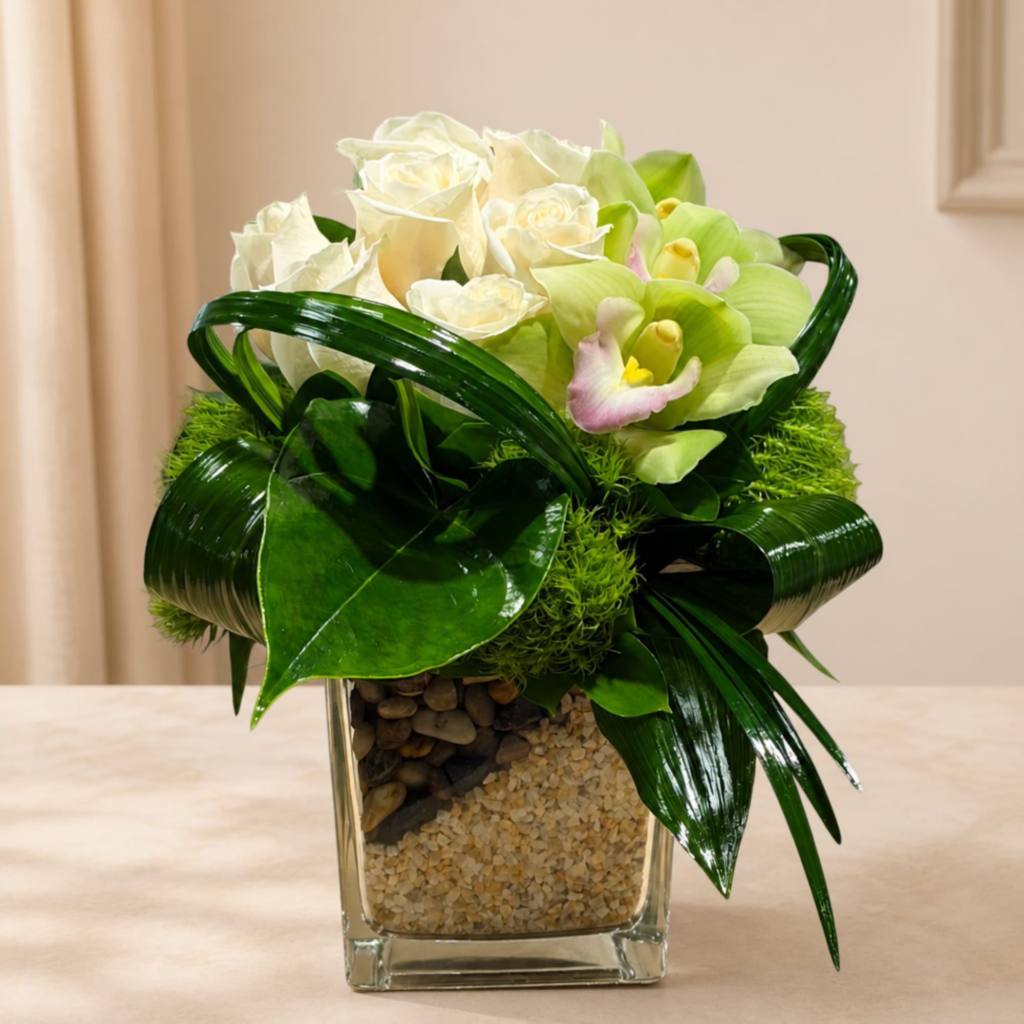 White roses and green orchids in a square glass vase with pebbles