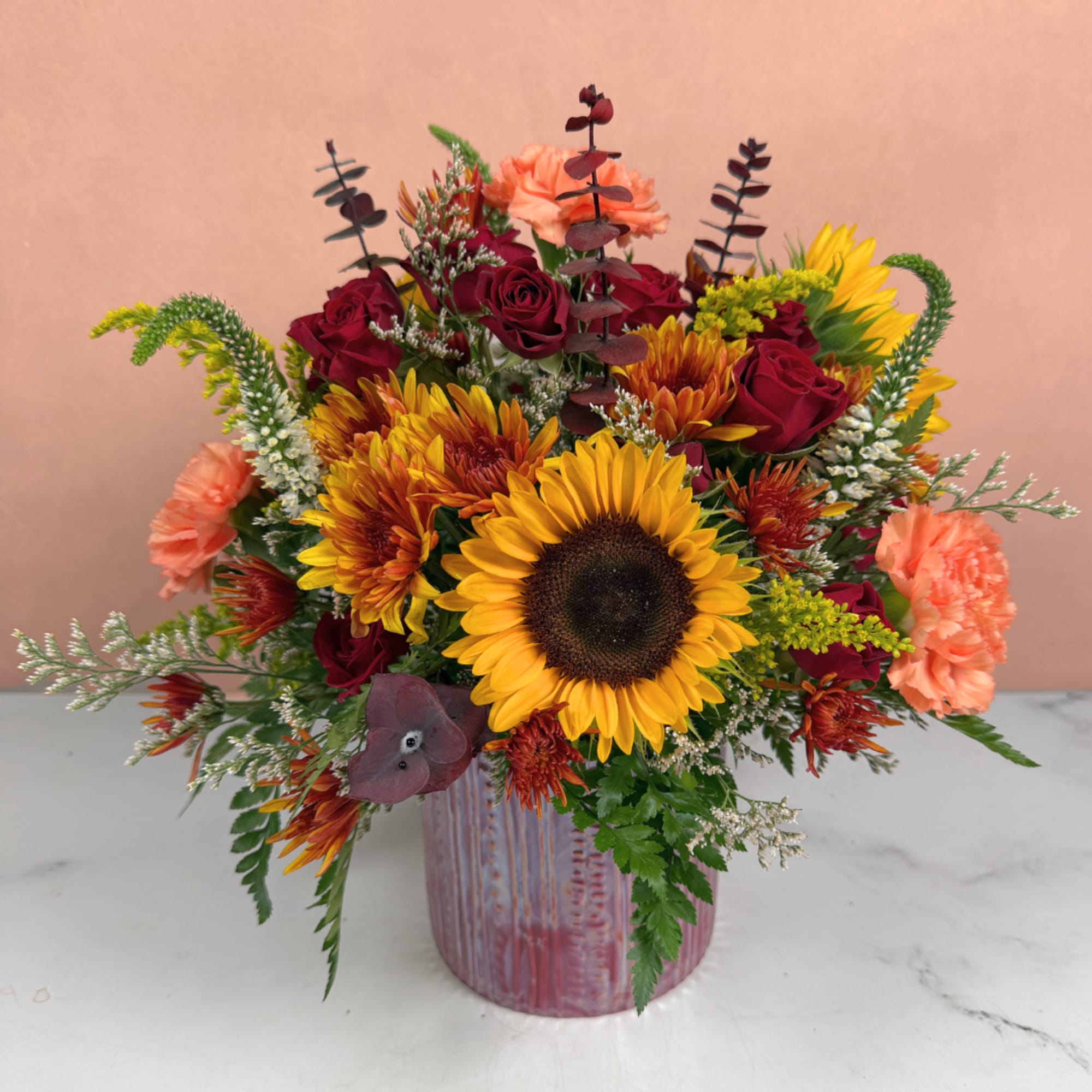 Mixed bouquet with sunflowers, red roses, and peach carnations in a pink vase, photo 2 of 4
