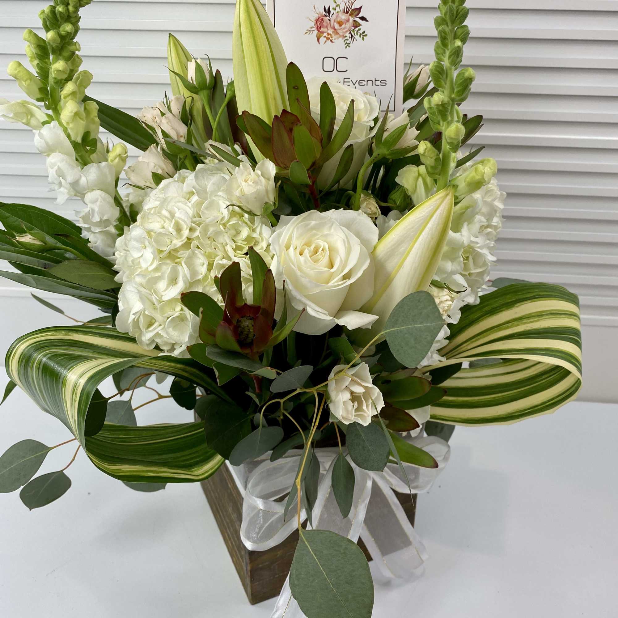 White floral arrangement with roses, hydrangeas, and lilies in a wooden box